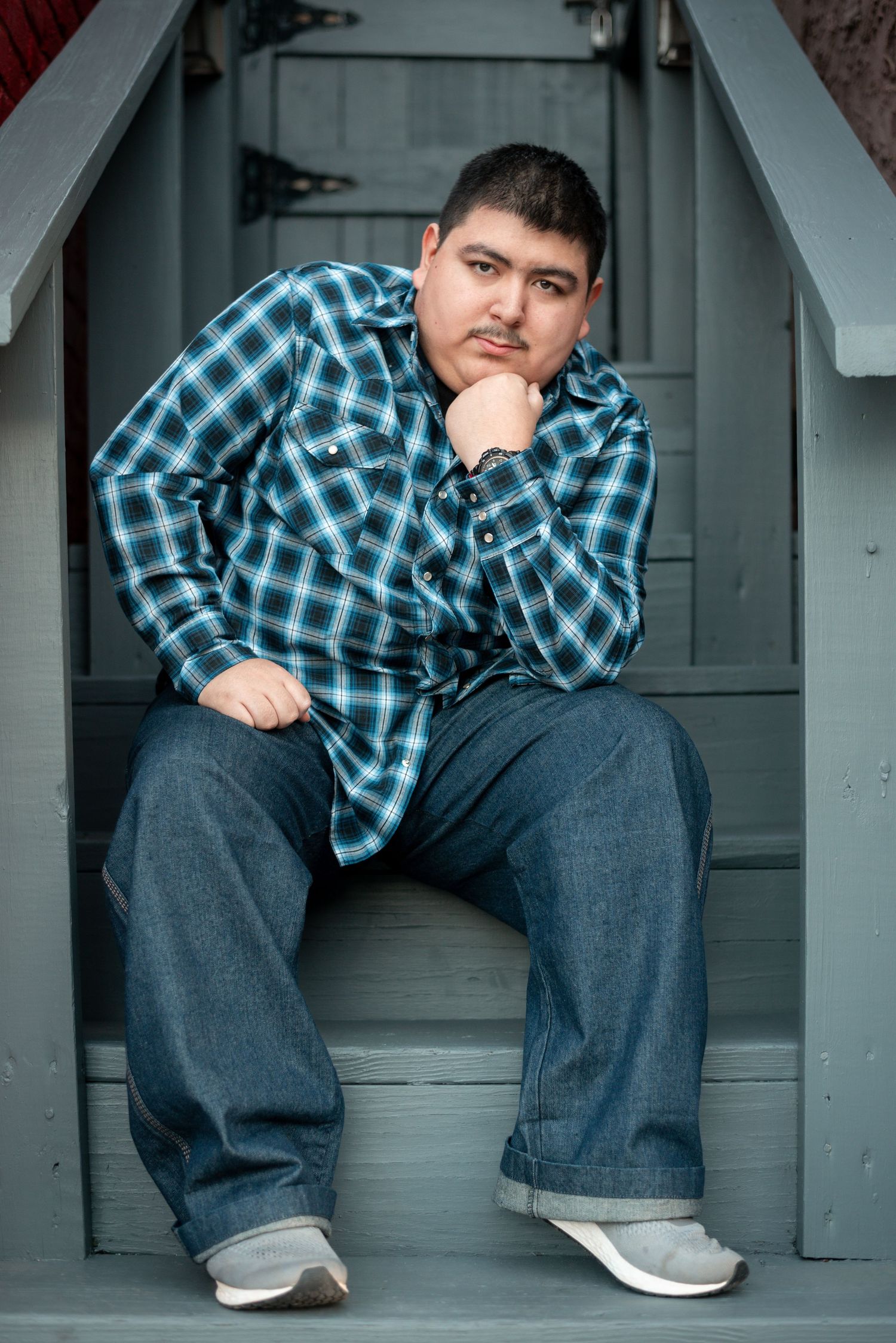 Person in plaid shirt sitting on gray steps in casual pose.