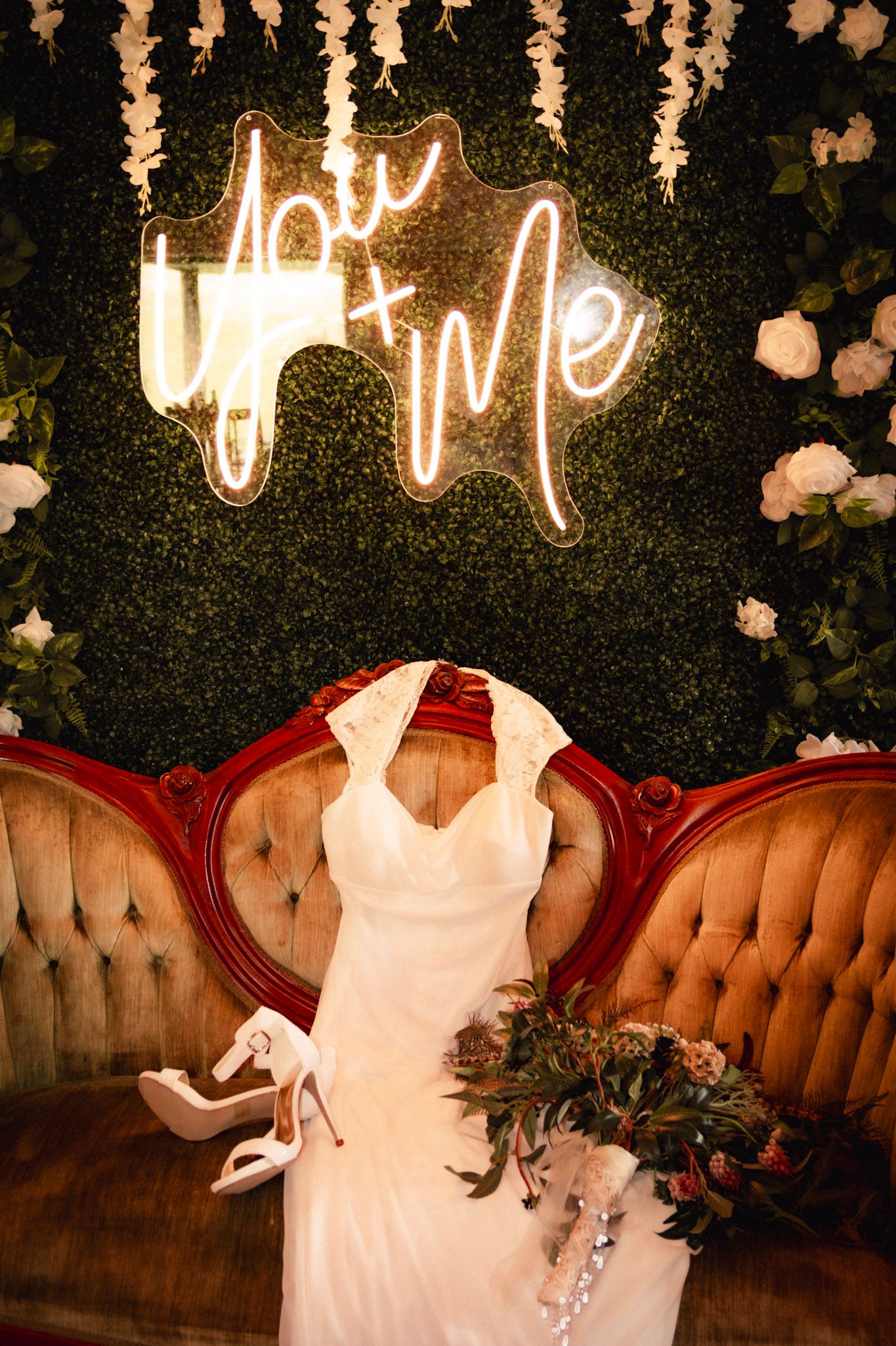 Wedding decor with neon signage and vintage tufted seating against a floral backdrop.