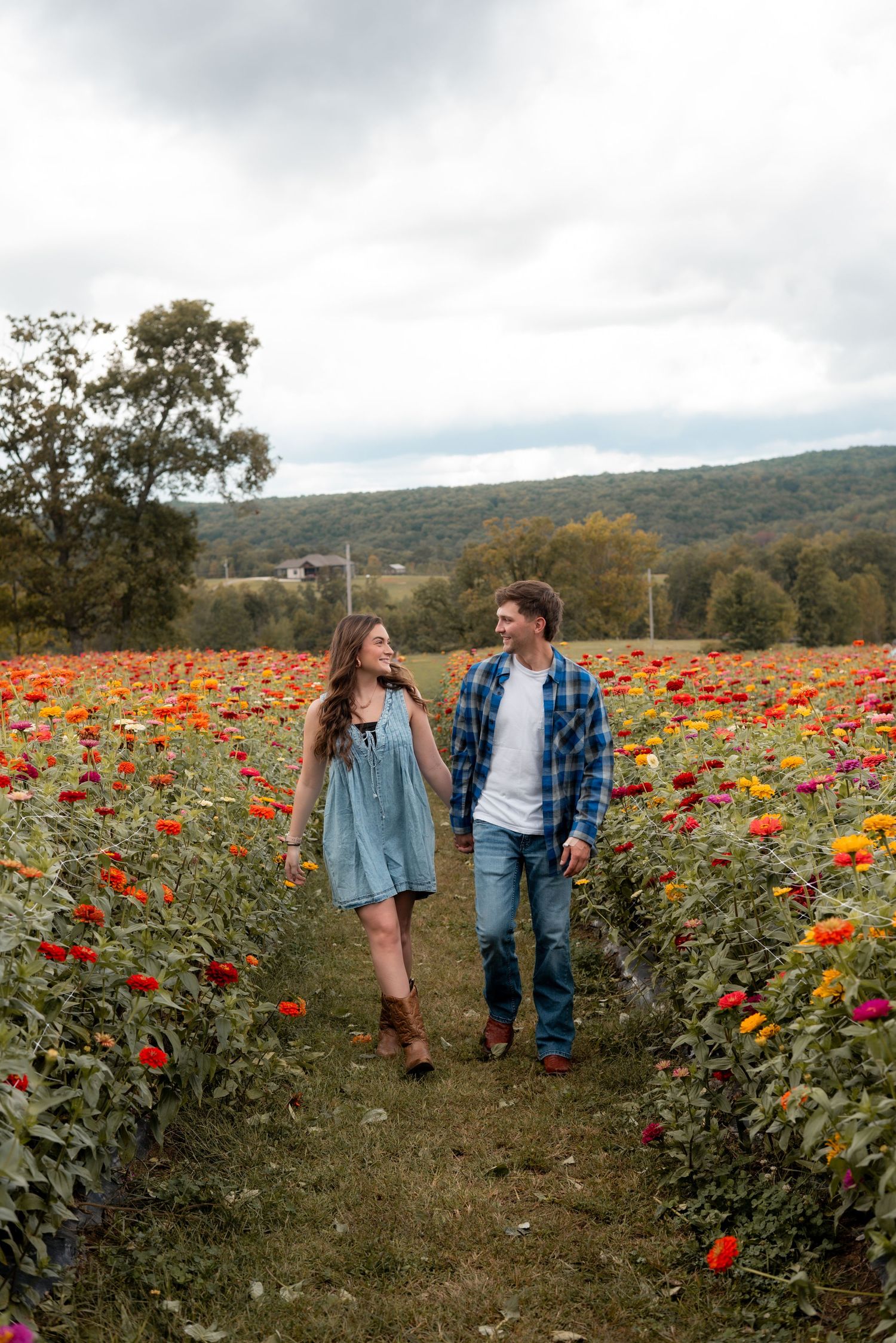 A couple walks through a vibrant flower field filled with colorful blooms on a cloudy day.