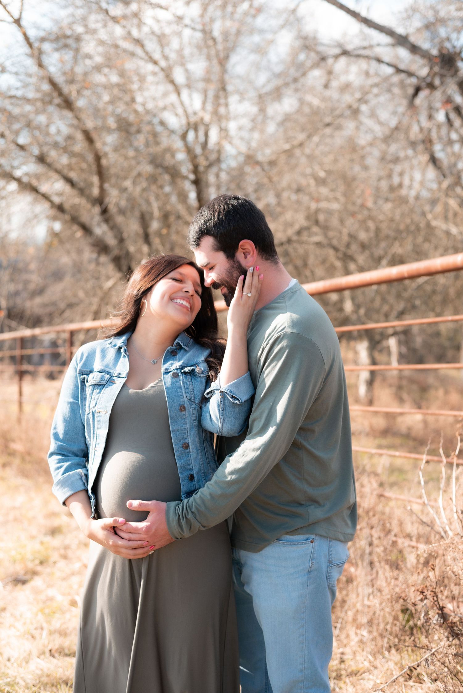 Intimate maternity photo of couple in casual denim and gray clothing outdoors.