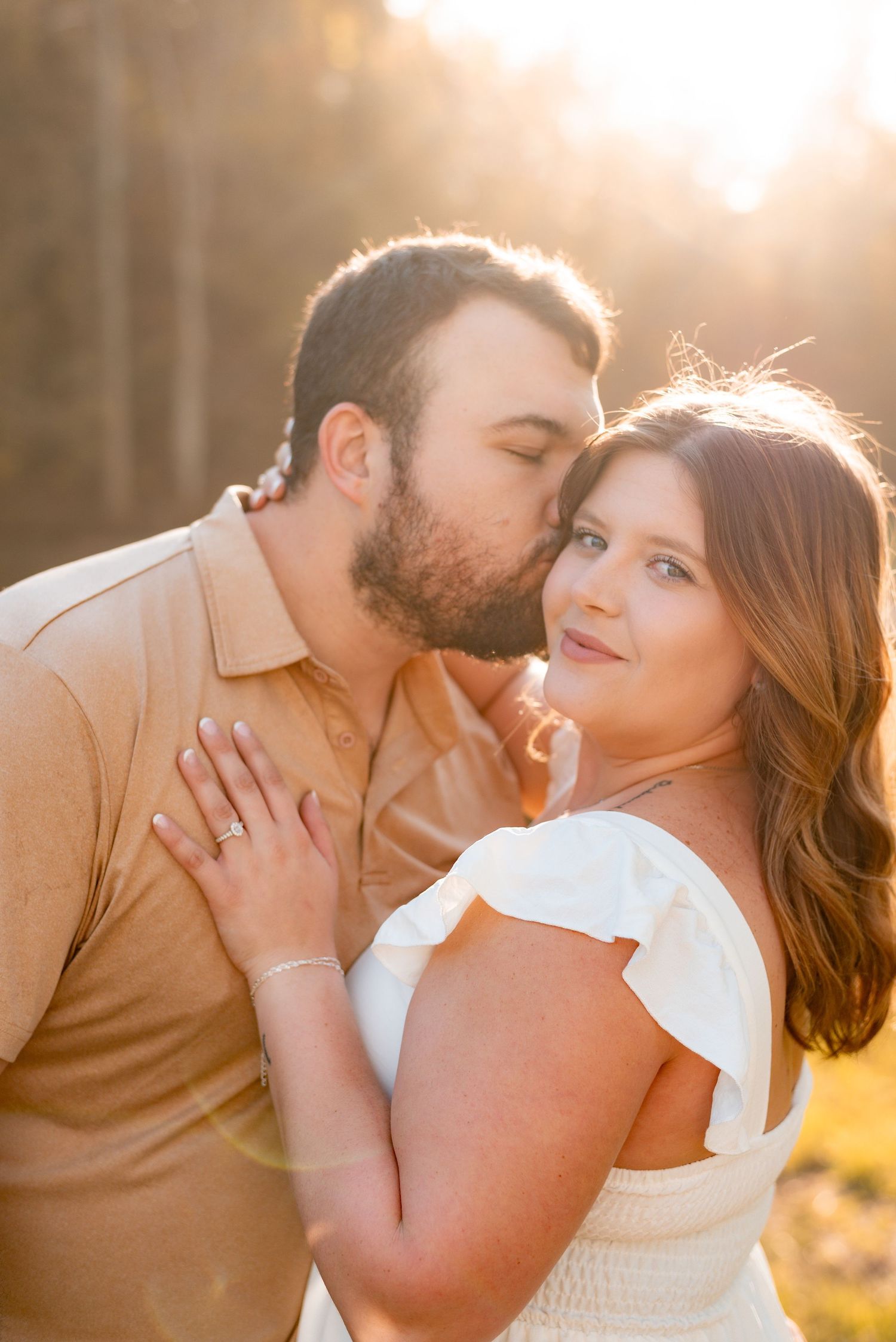 Romantic couple sharing intimate moments during golden hour sunset photoshoot in a field.