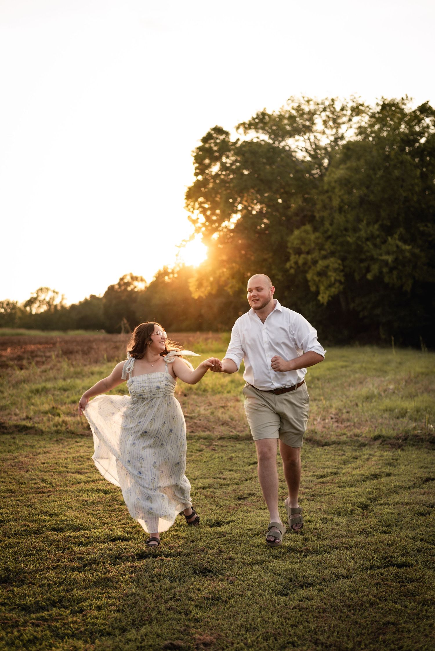 Couple running and playing together on grassy hillside at sunset.