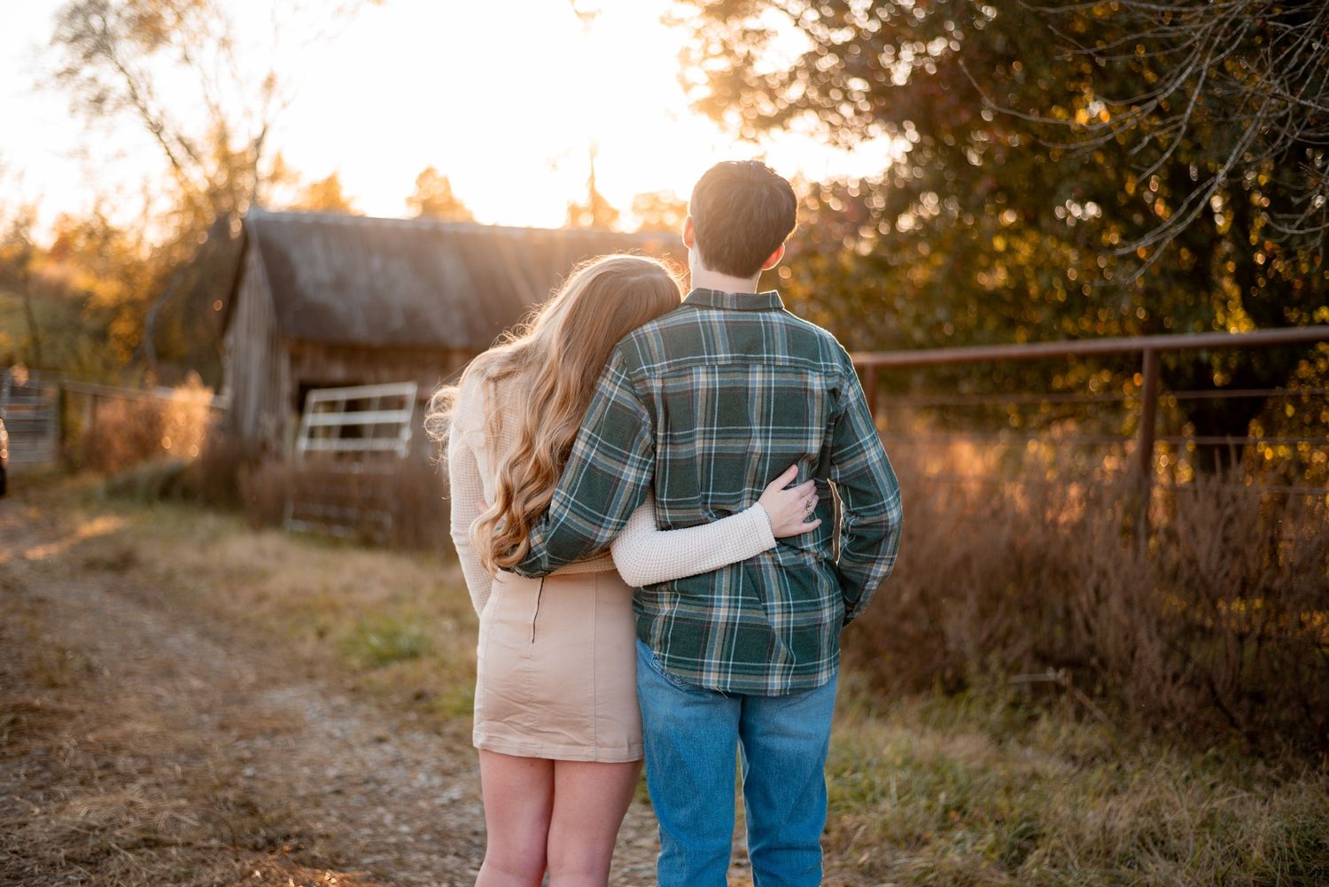 A couple walks hand in hand along a rural path at sunset.