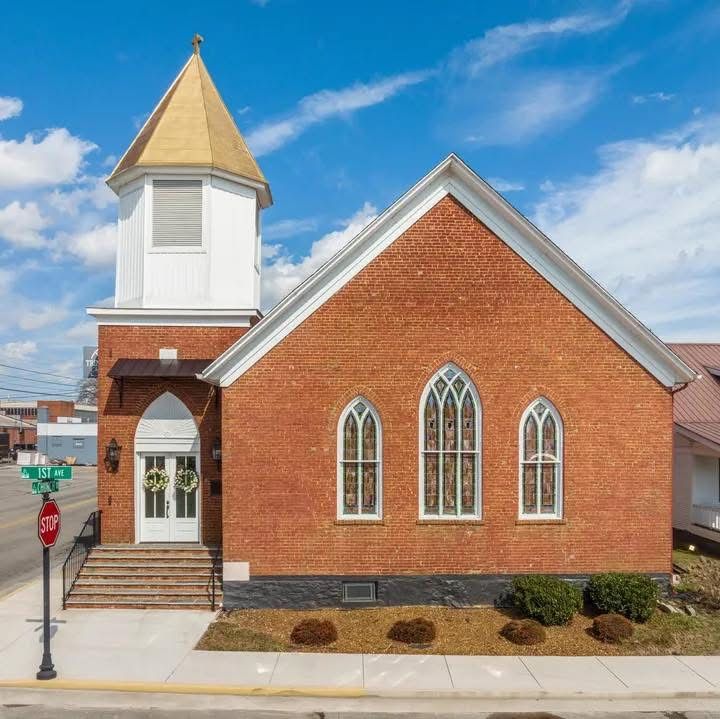 Historic red brick church with Gothic arched windows, white bell tower with gold steeple, and stone steps under blue sky.