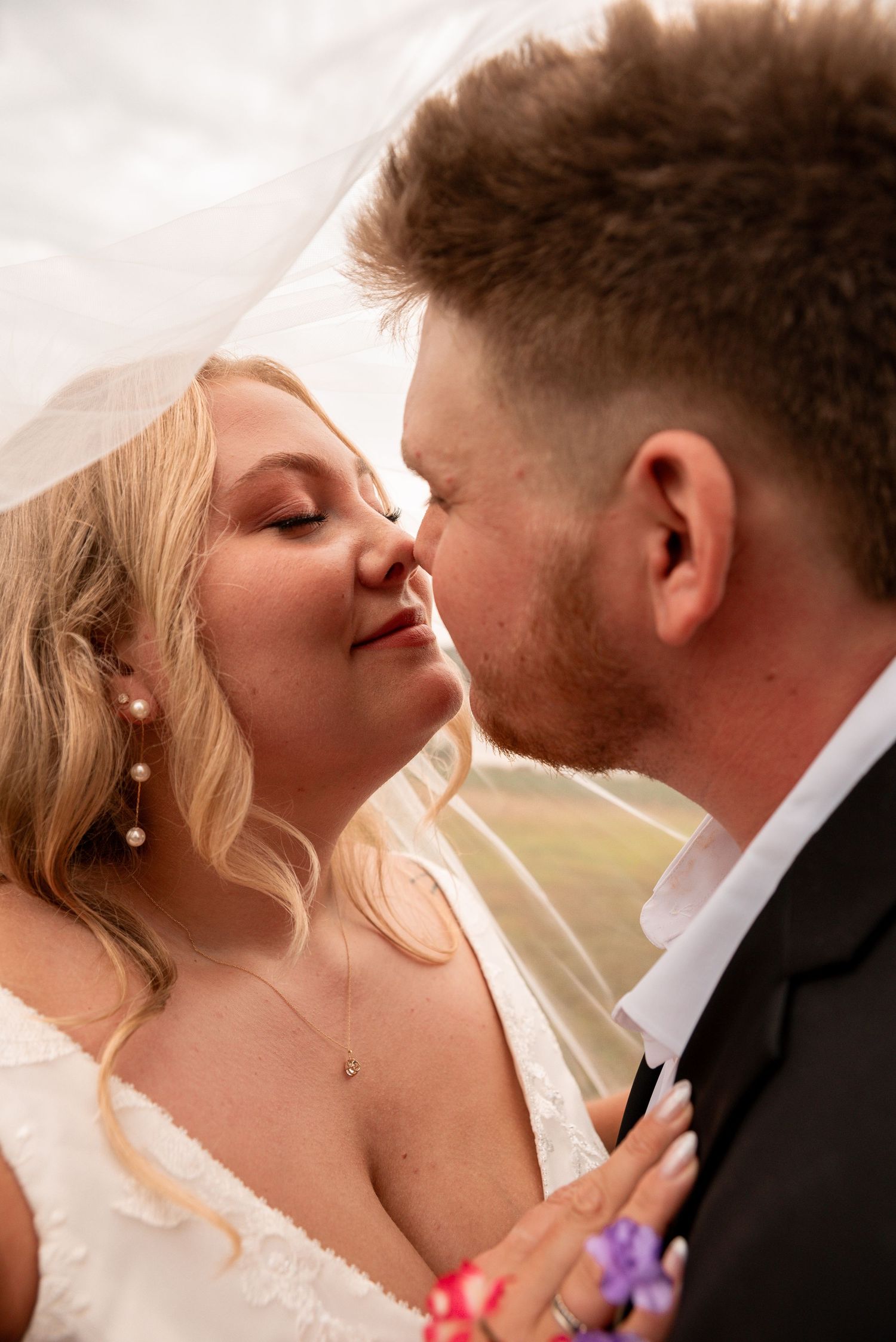 A bride and groom share a tender kiss under a flowing white veil on their wedding day.