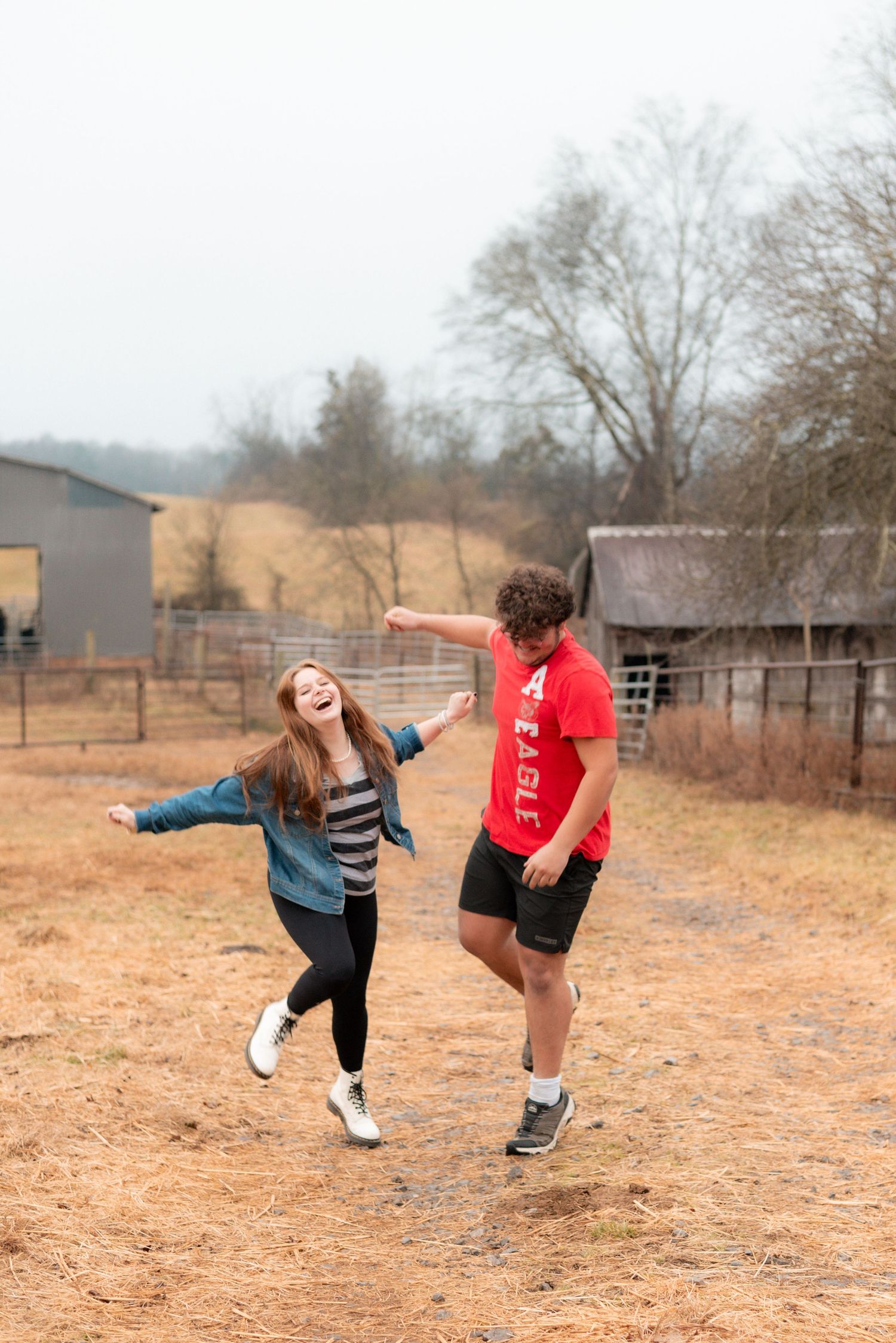 Couple having fun doing silly poses in an open field with farm buildings in the background.