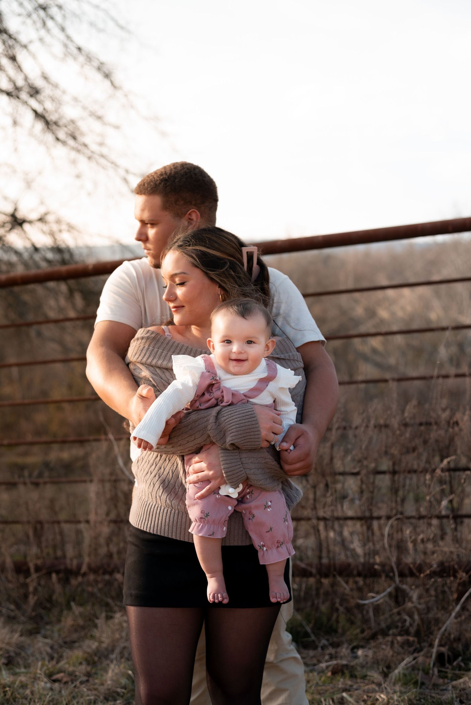 Happy baby smiling while being held near wooden fence at sunset.
