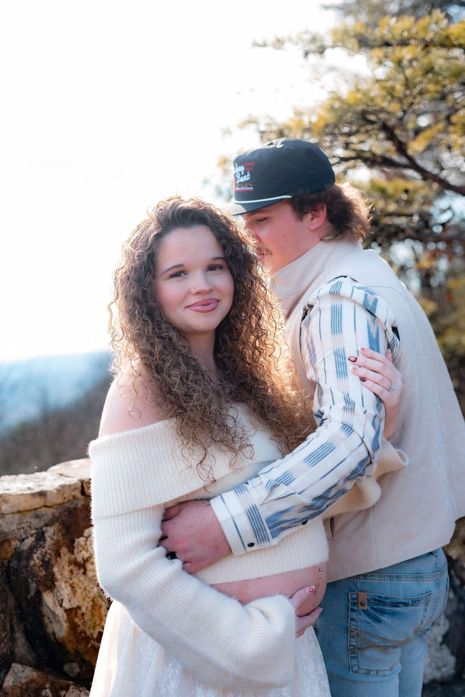 Romantic outdoor maternity photo of couple embracing against autumn backdrop.