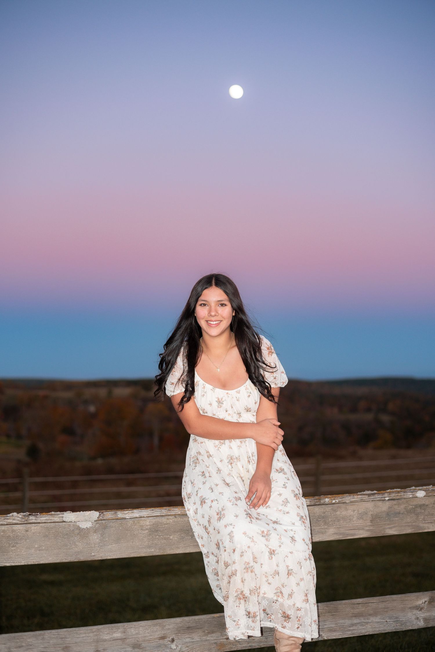 A white floral dress catches the light during a sunset photoshoot with the moon visible in the sky.