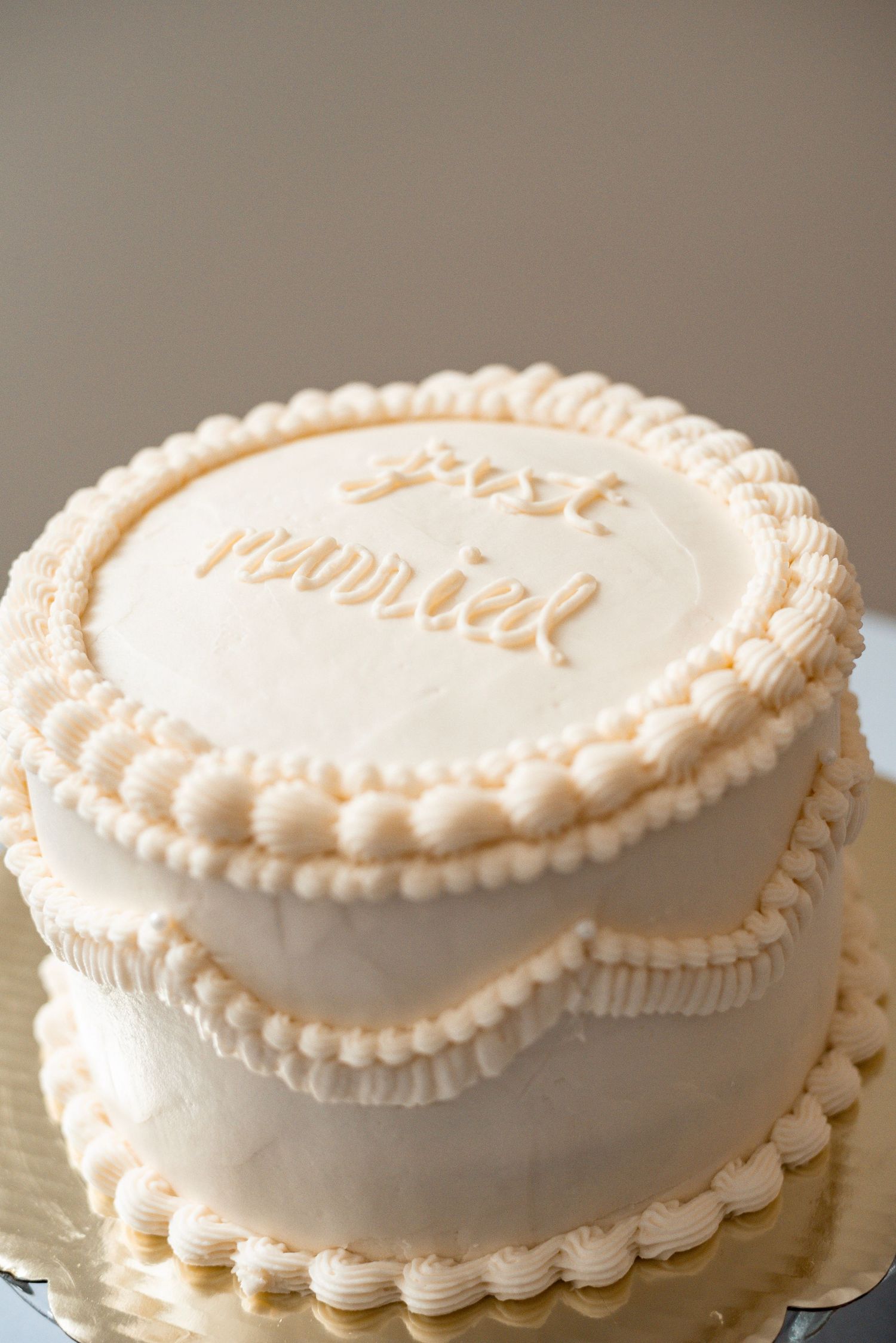 Elegant two-tier white buttercream cake with pearl borders and 'post nuptial' script topping.