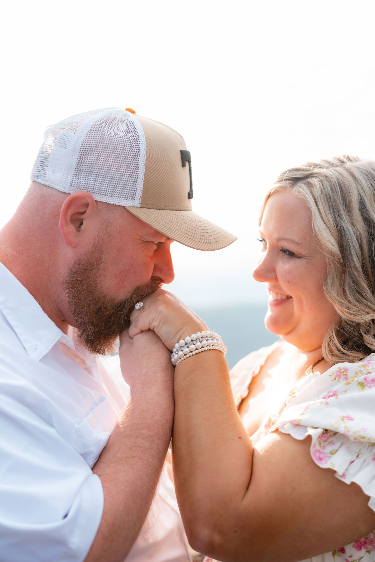 A couple shares a romantic moment as the man kisses the woman's hand outdoors in golden backlight.