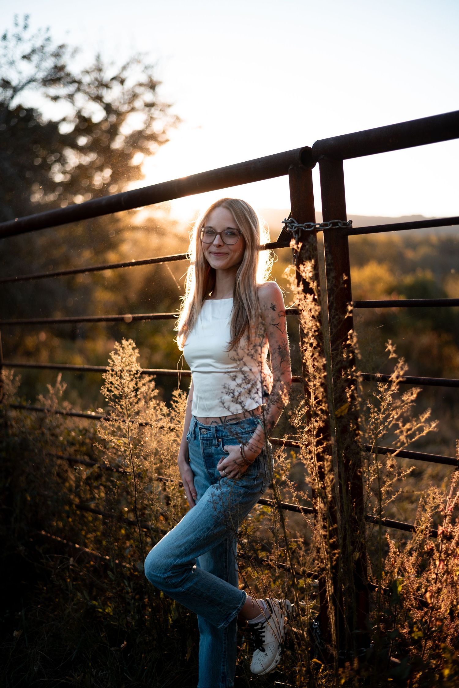 Artistic portrait at golden hour with sunlit grass and metal railings in the background.