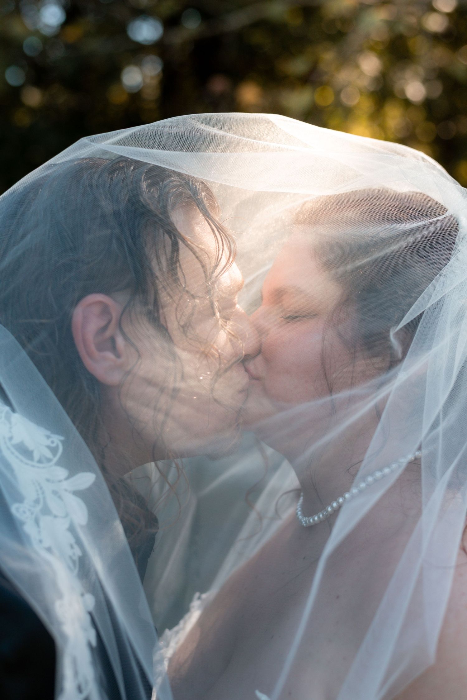 Romantic wedding kiss captured through delicate white veil with bokeh background.