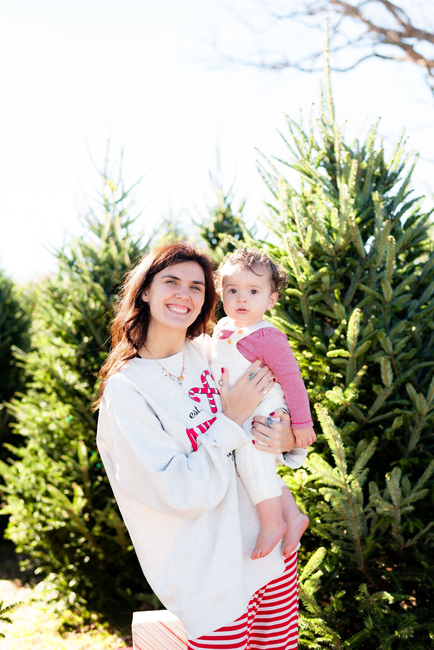 Mother and baby in matching white and red outfits at Christmas tree farm.