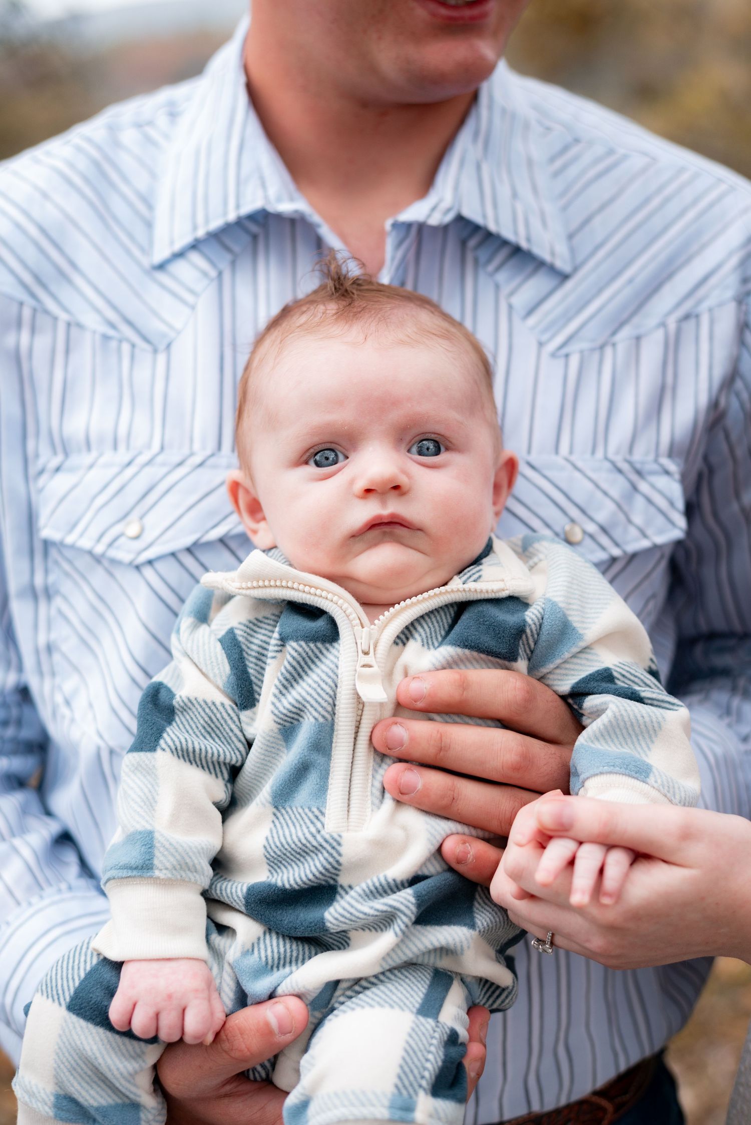 Baby in striped outfit being held against outdoor background.