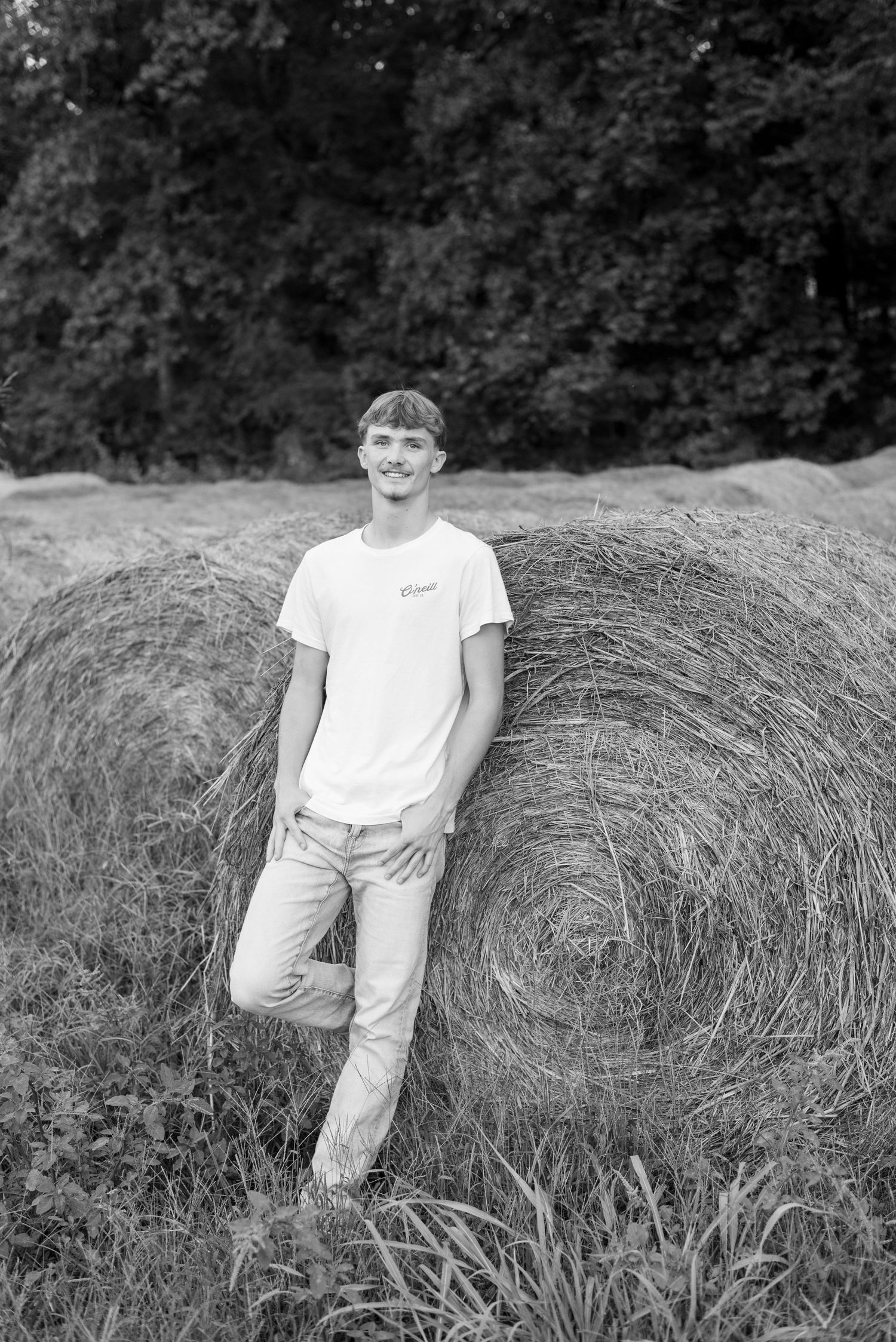 Person in white t-shirt poses casually on large hay bale in black and white photo.
