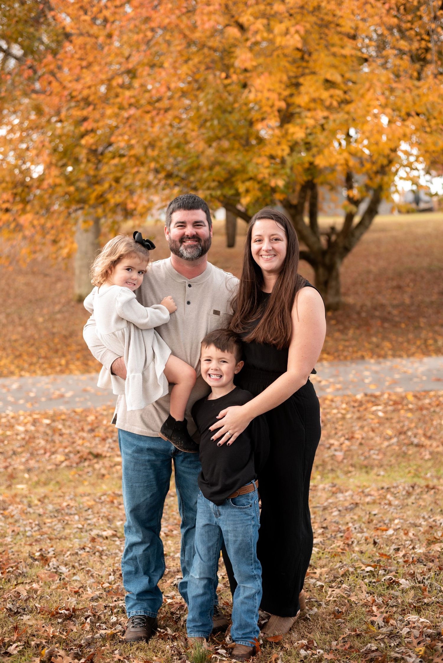 A family poses playfully together on fallen autumn leaves with trees in the background.