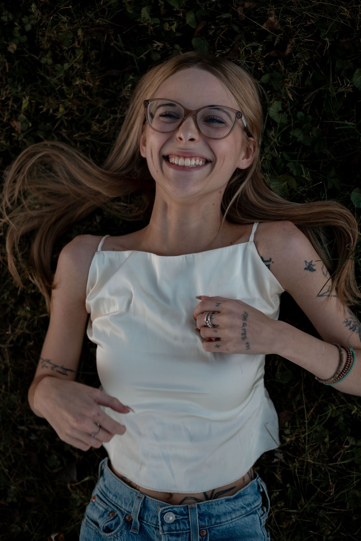 Joyful lying down portrait on grass wearing glasses and a white top at sunset.