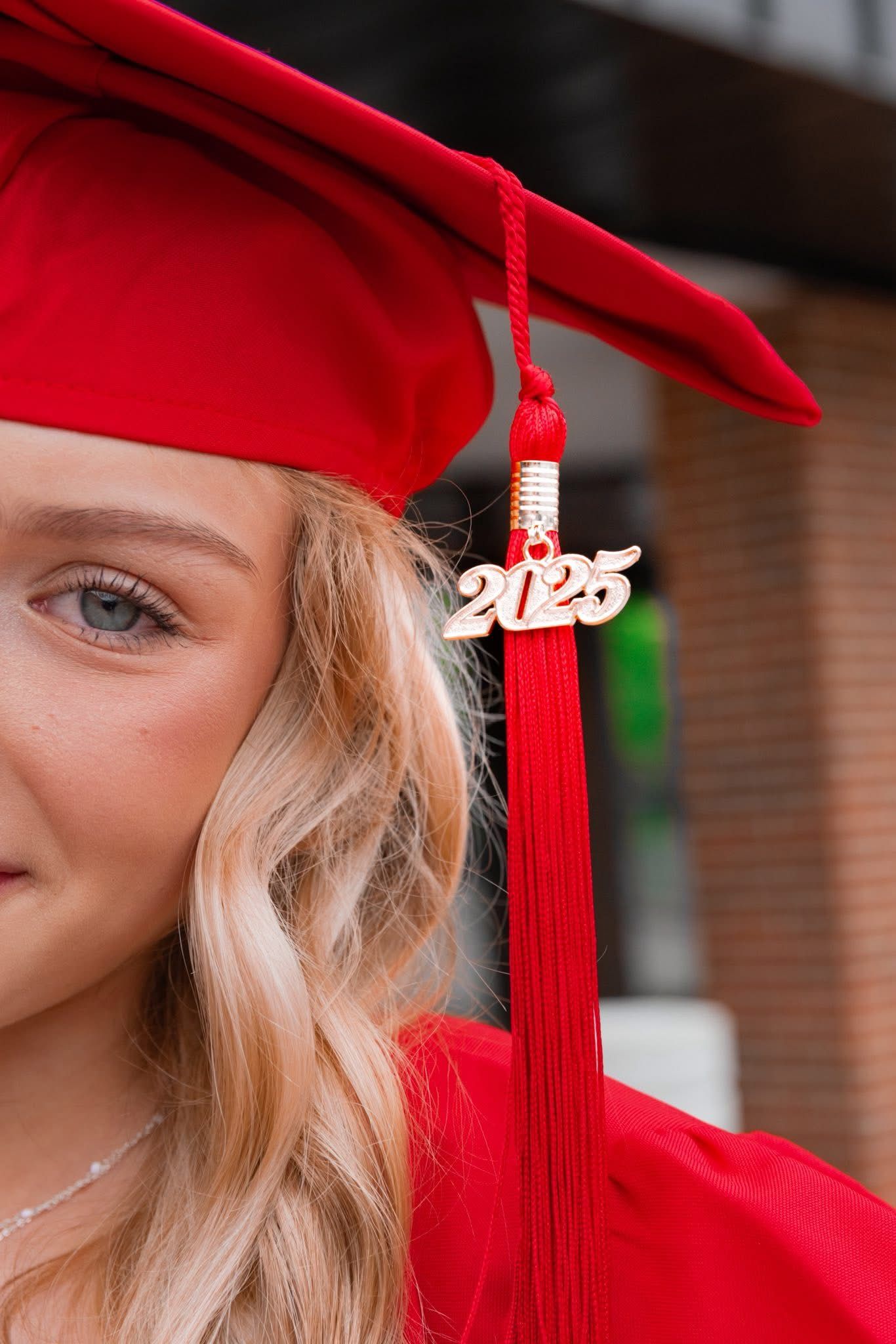 Close-up of red graduation cap with tassel against brick building.
