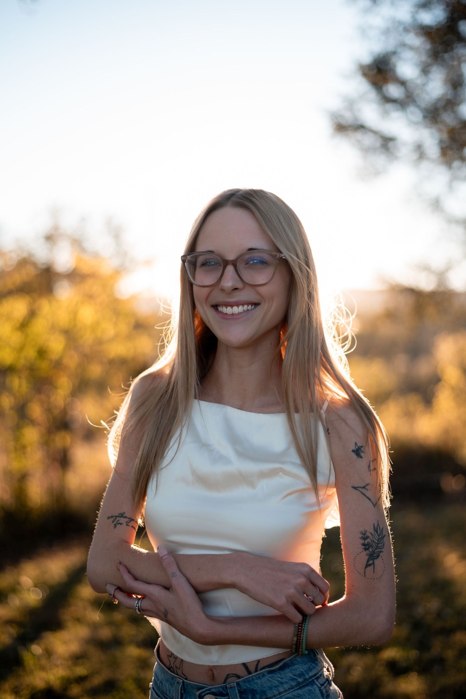 Candid sunset portrait featuring a white crop top and visible tattoos against golden hour lighting.