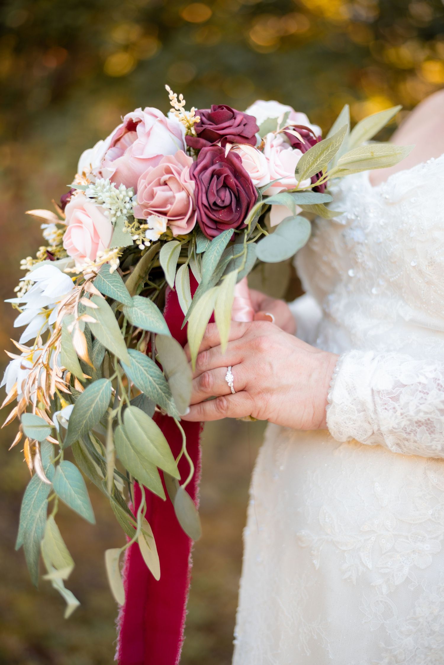 Close-up of elegant wedding bouquet with burgundy and pink roses wrapped in velvet ribbon.