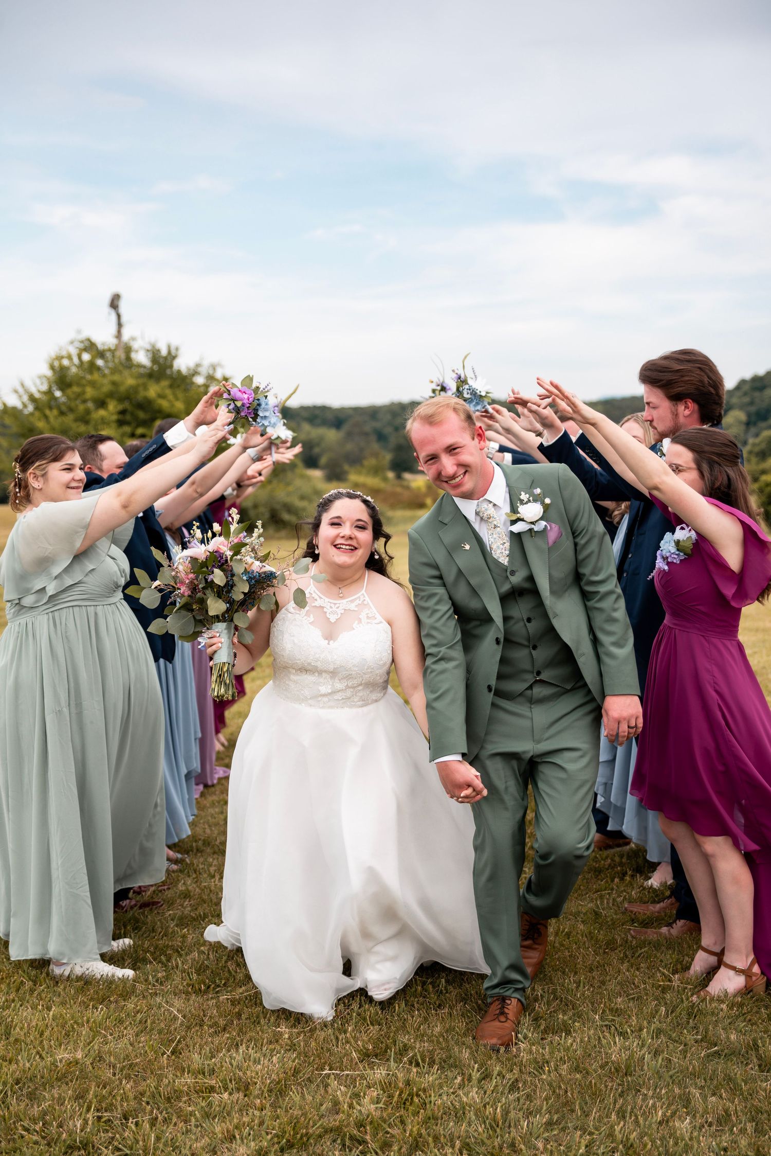 Bride and groom walk through an arch of raised hands formed by bridesmaids and groomsmen during outdoor wedding celebration.