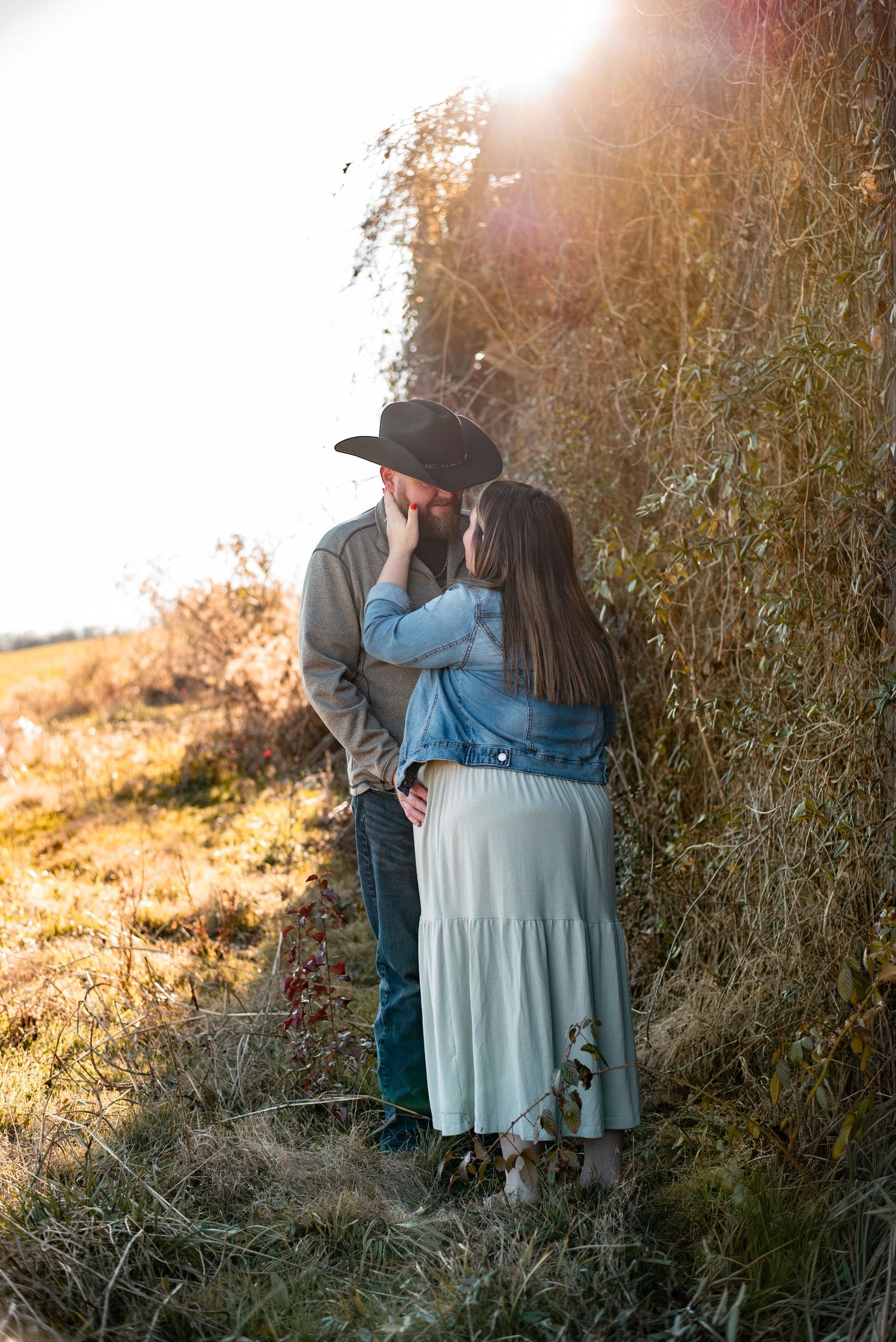 Romantic maternity photos taken at sunset with couple sitting together in tall grass.