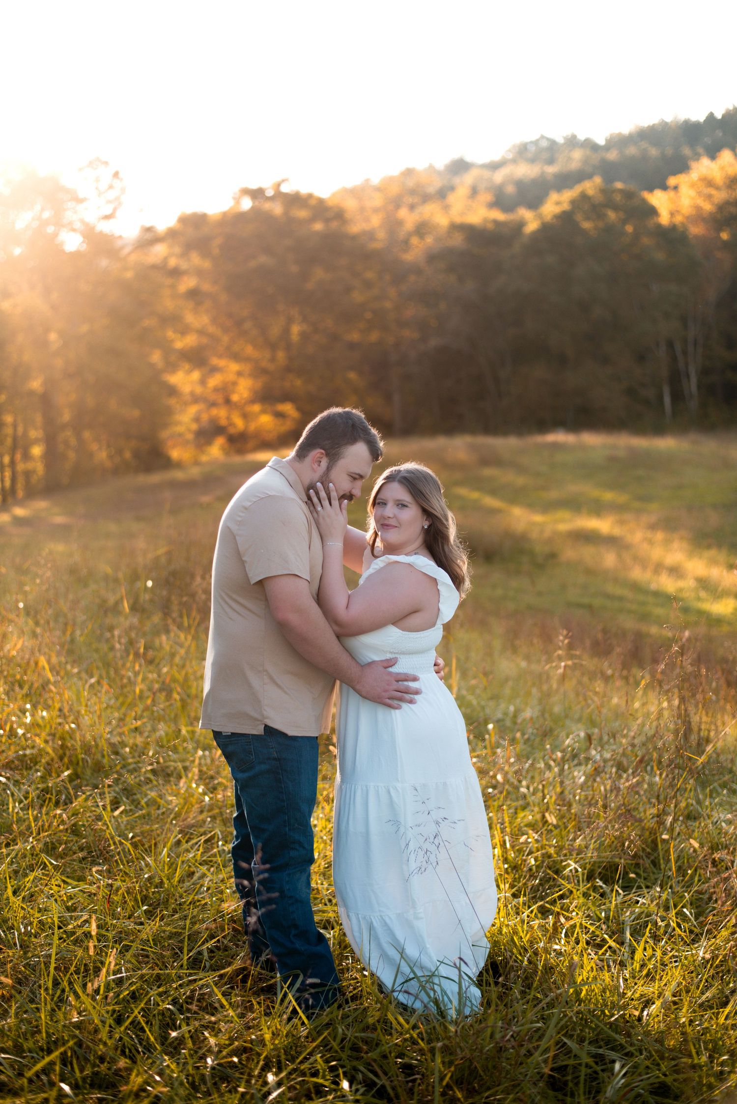 Couple embracing in tall grass during golden hour photography session.