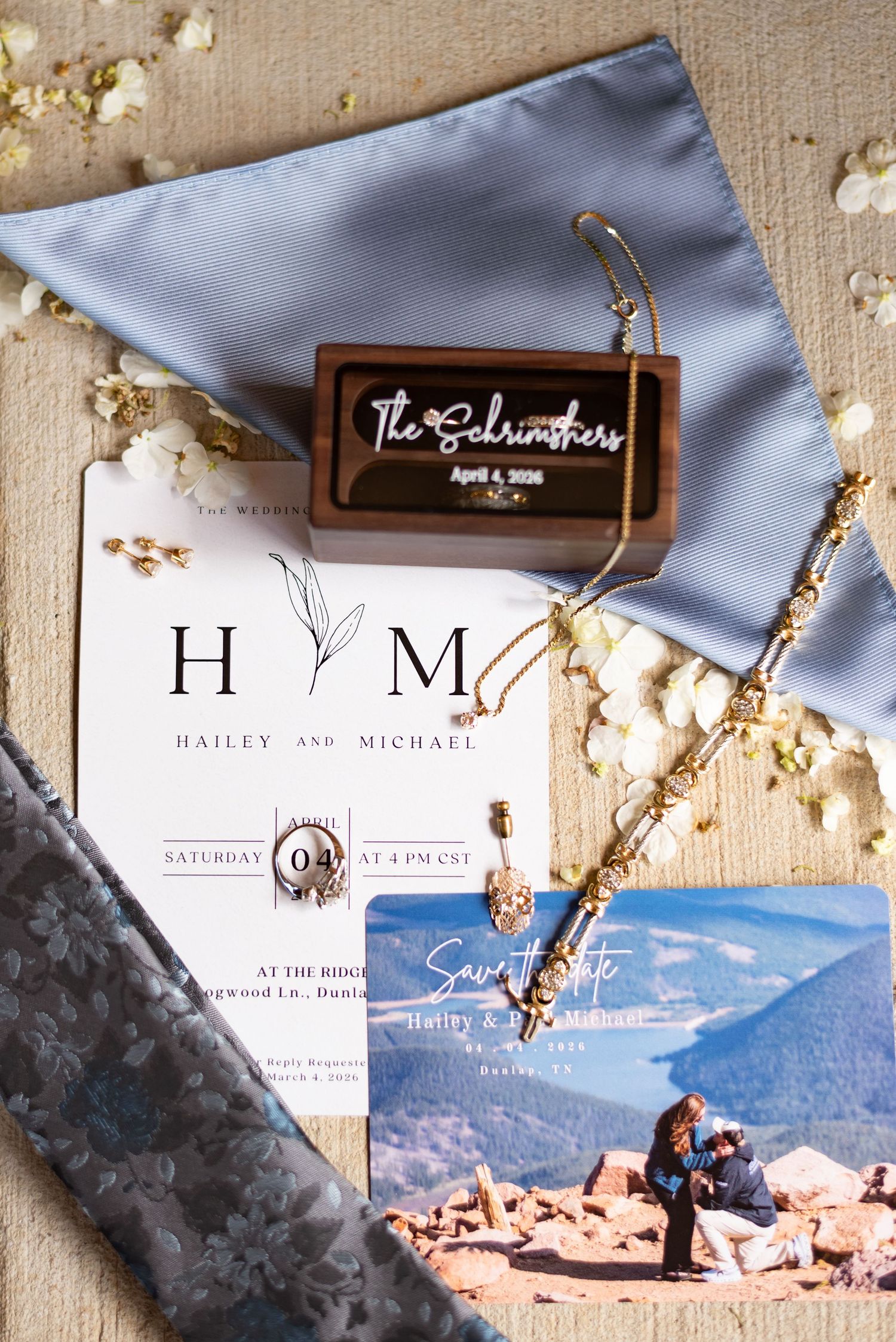 Wedding flat lay featuring Hailey and Michael's invitation suite, save the date, gold jewelry, and personalized wooden ring box.