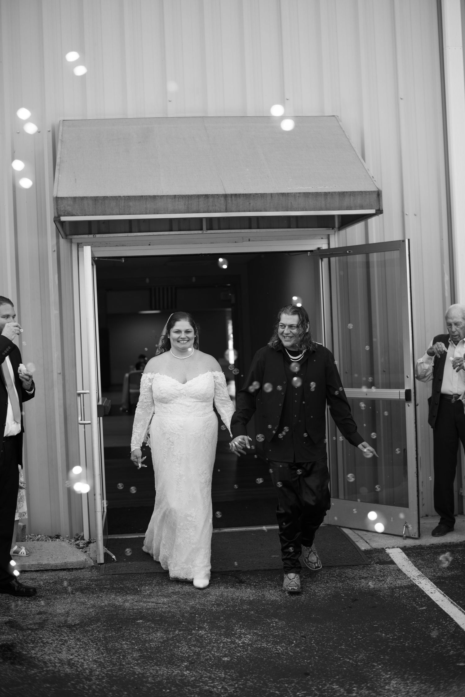 A bride in a white wedding dress exits a building at night surrounded by guests.