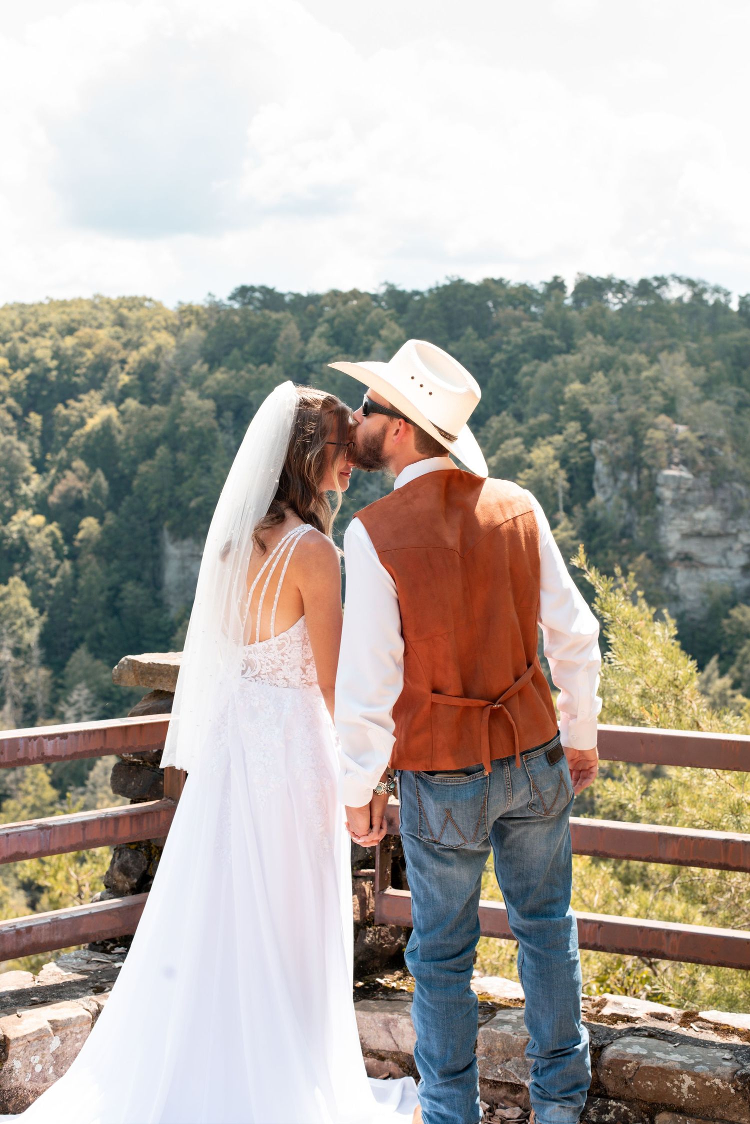 Scenic wedding photos overlooking a mountain valley with couple at wooden railing.