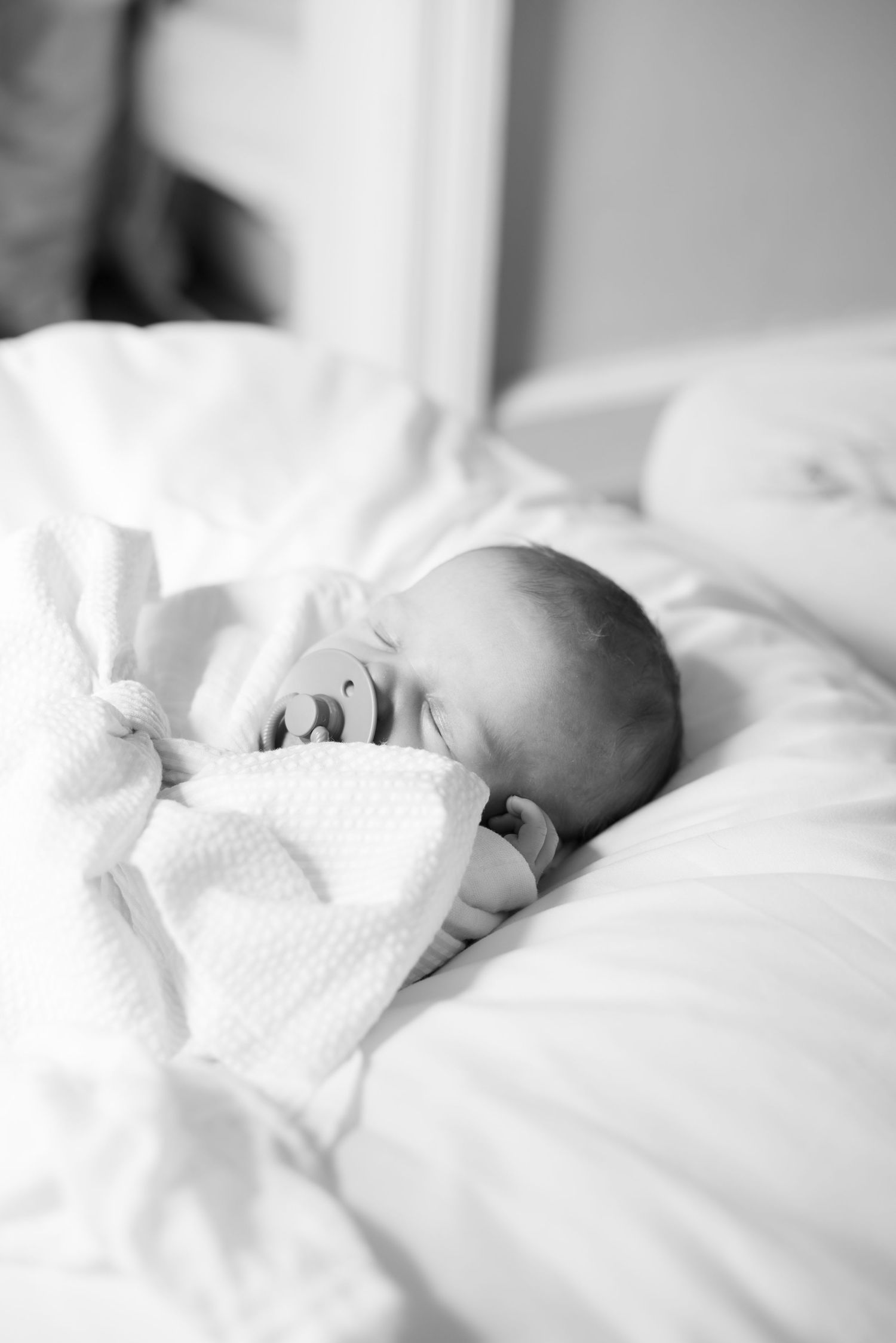 Peaceful newborn sleeping in soft white bedding captured in black and white.