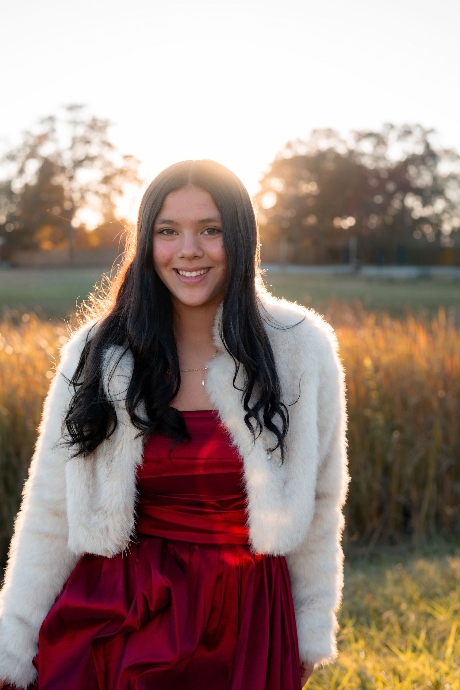 Portrait in a red velvet dress and white fur jacket against a golden sunset field.