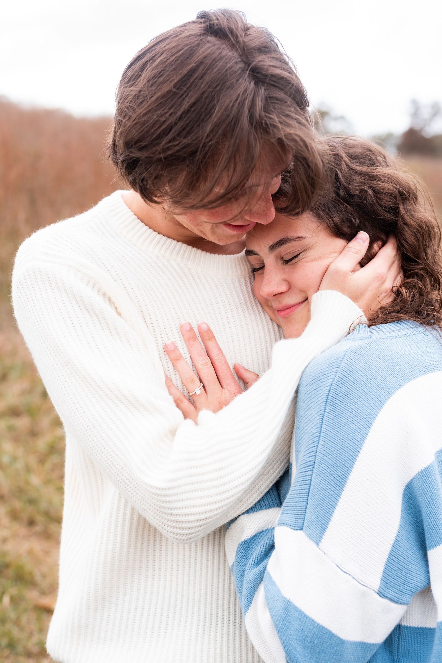 A romantic couple embraces while wearing white and blue sweaters against a blurred background.