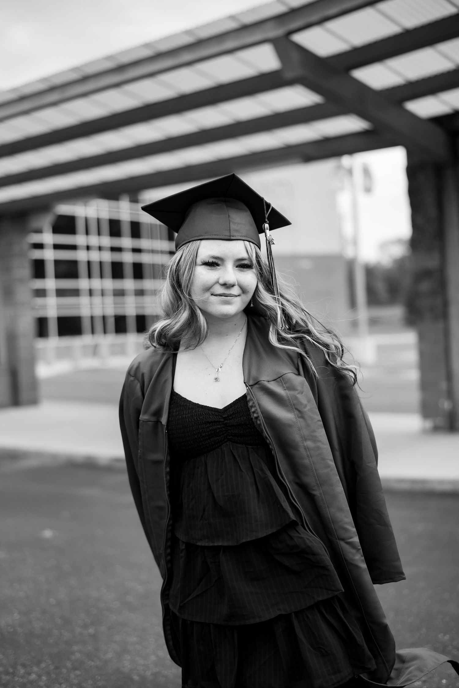 Young woman in graduation cap and gown smiling outdoors in black and white photo.
