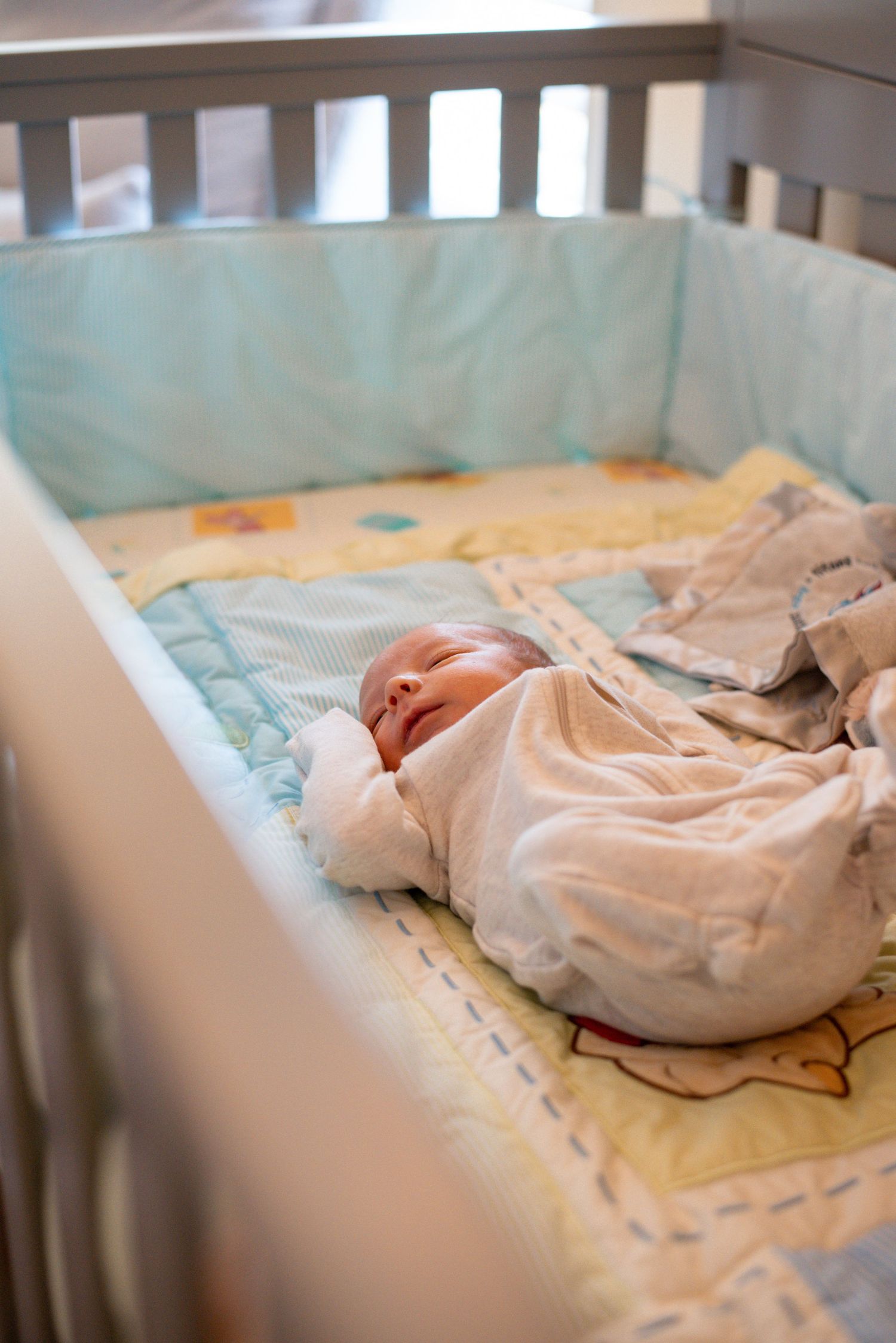Sleeping newborn baby rests peacefully in white crib with soft bedding.