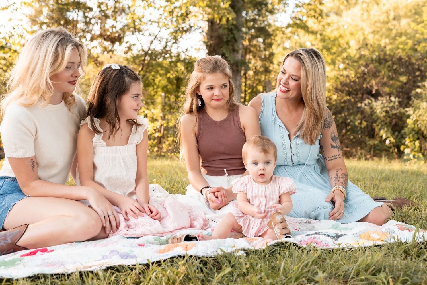 Family members relax on picnic blanket during outdoor photo session at sunset.