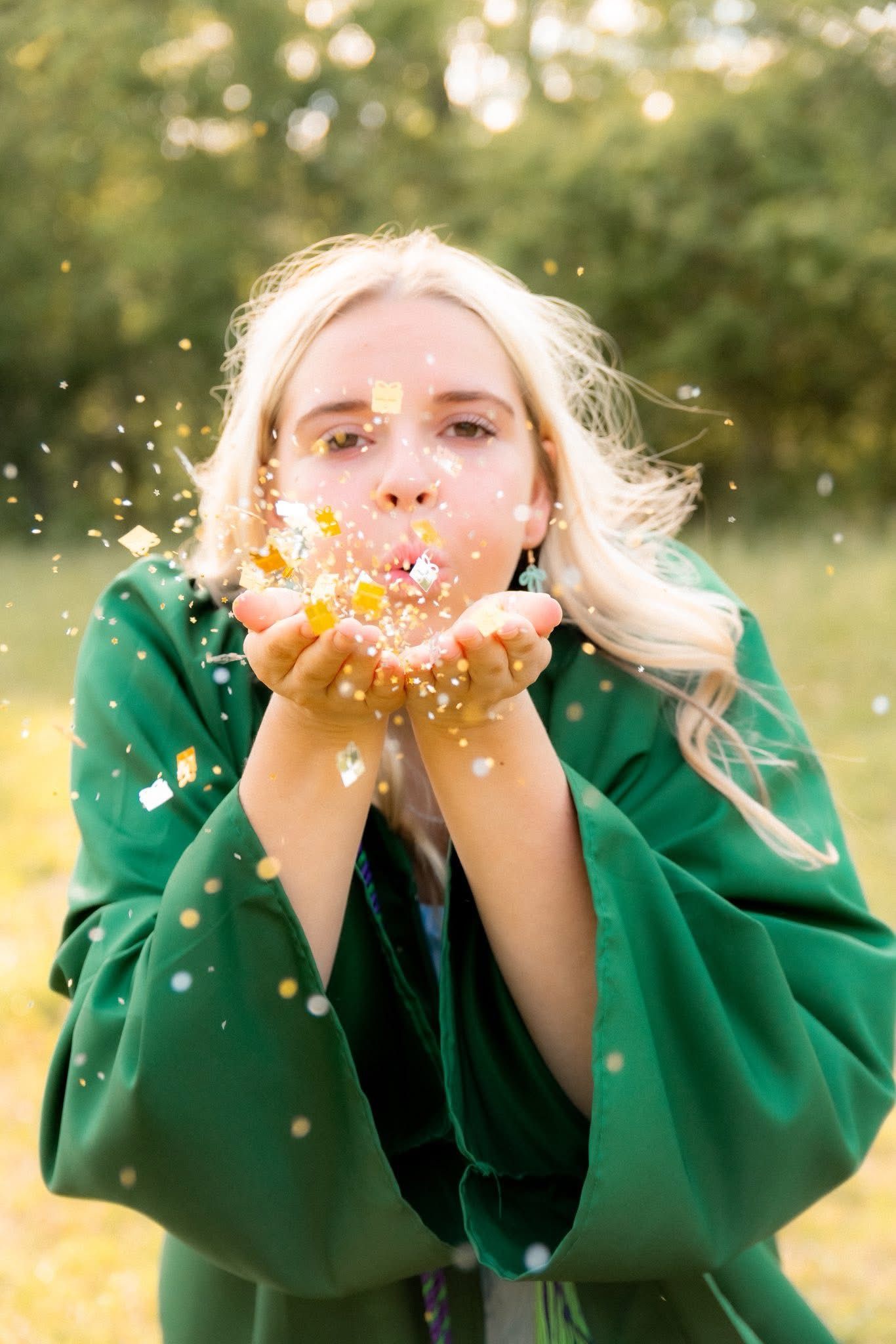 Person in green sweater blowing glitter in sunlit outdoor setting.