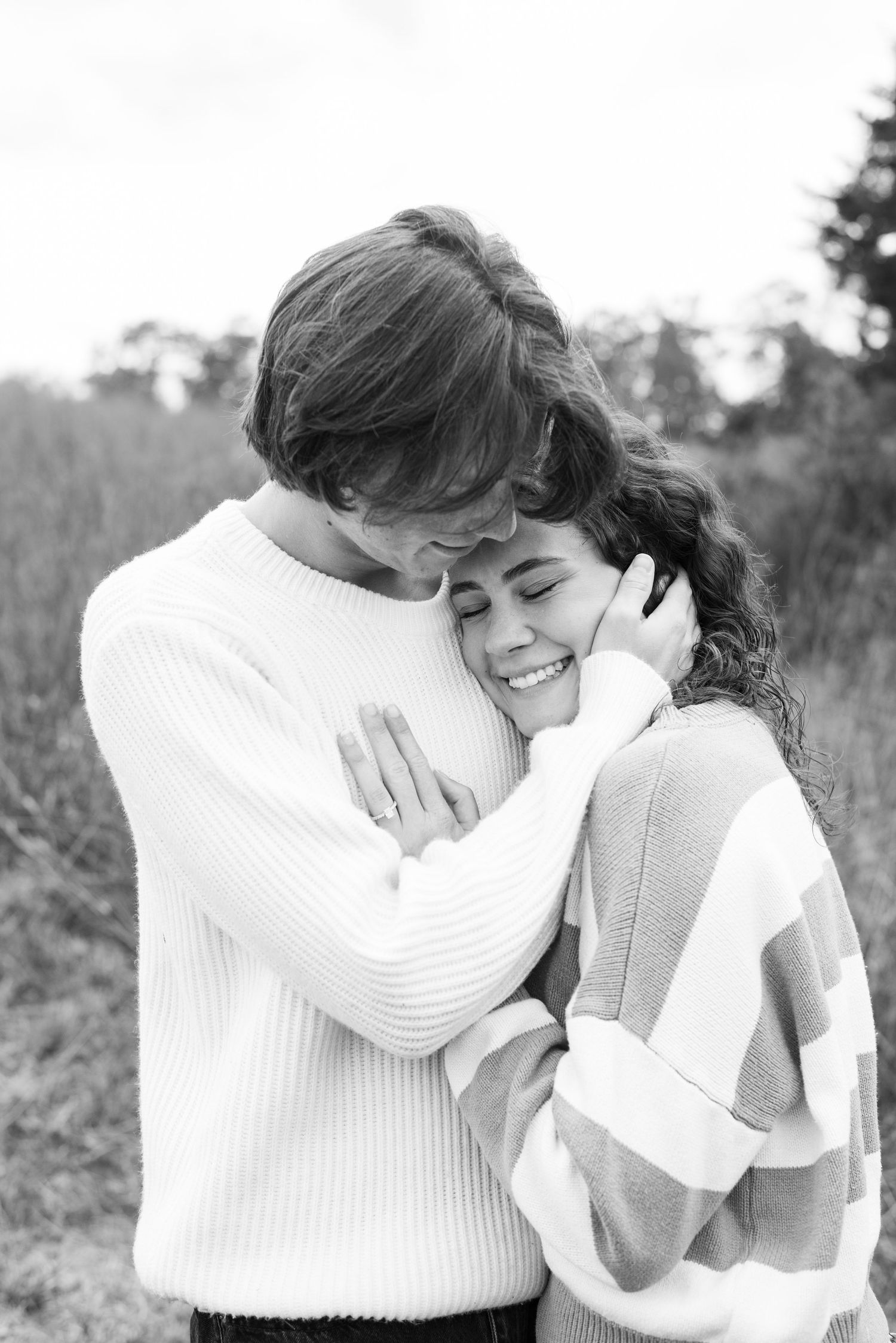 Black and white engagement photos of couple embracing in cozy sweaters.