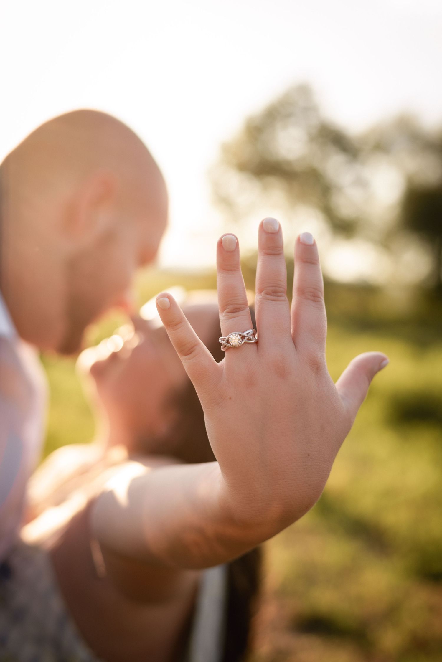 Hands displaying engagement ring against sunset backdrop.