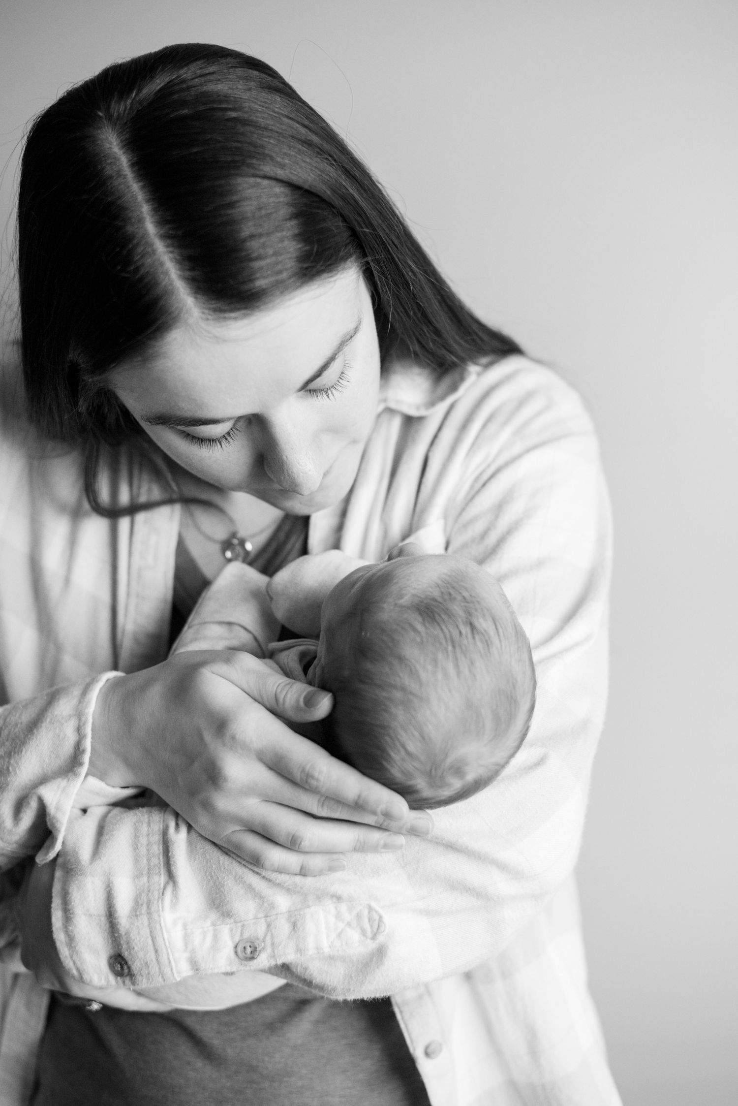 Mother in white gently cradles and kisses newborn baby in black and white portrait.