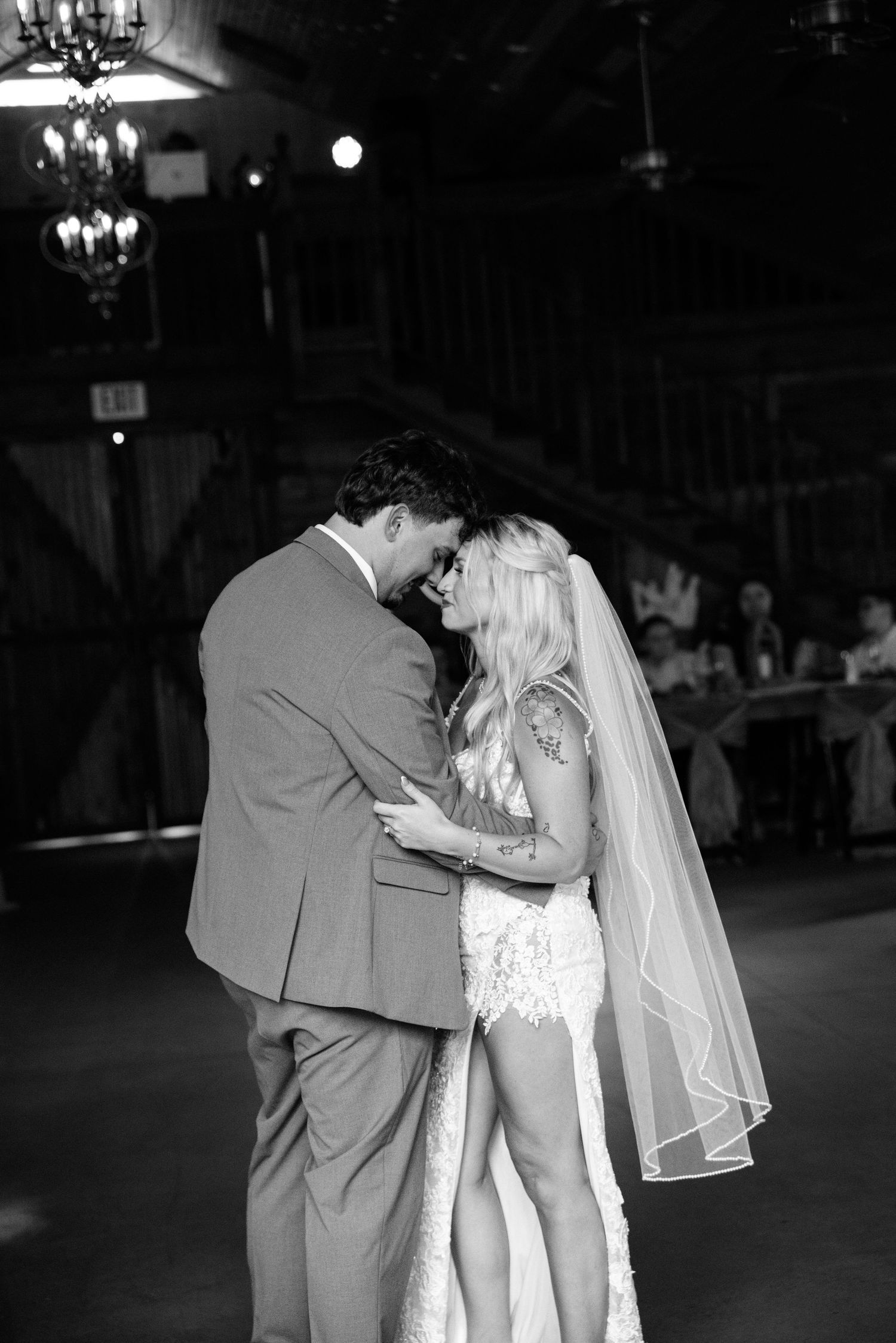 Black and white photo of bride and groom sharing first dance at rustic barn wedding reception.