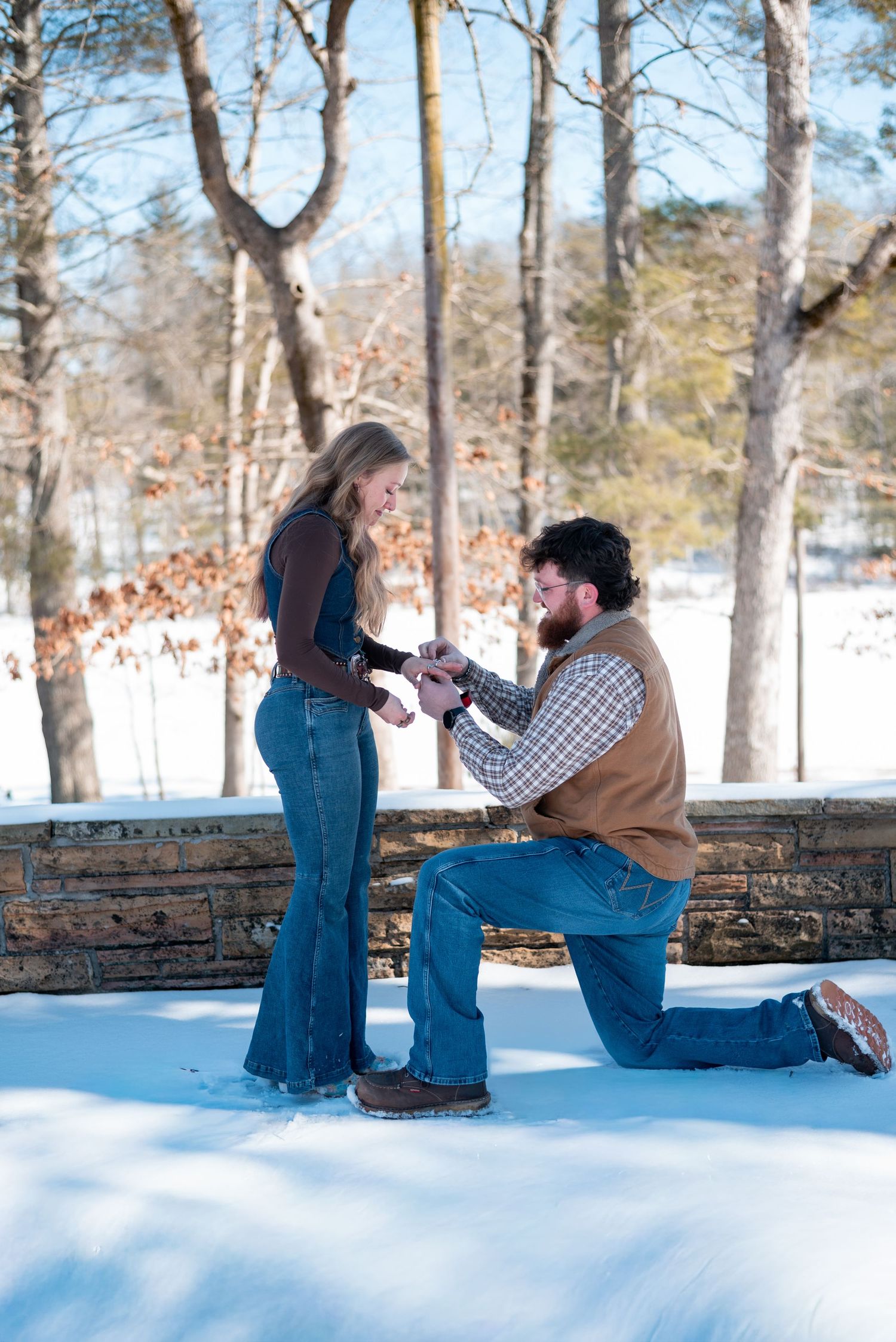 A winter proposal scene with snow-covered ground and bare trees in background.