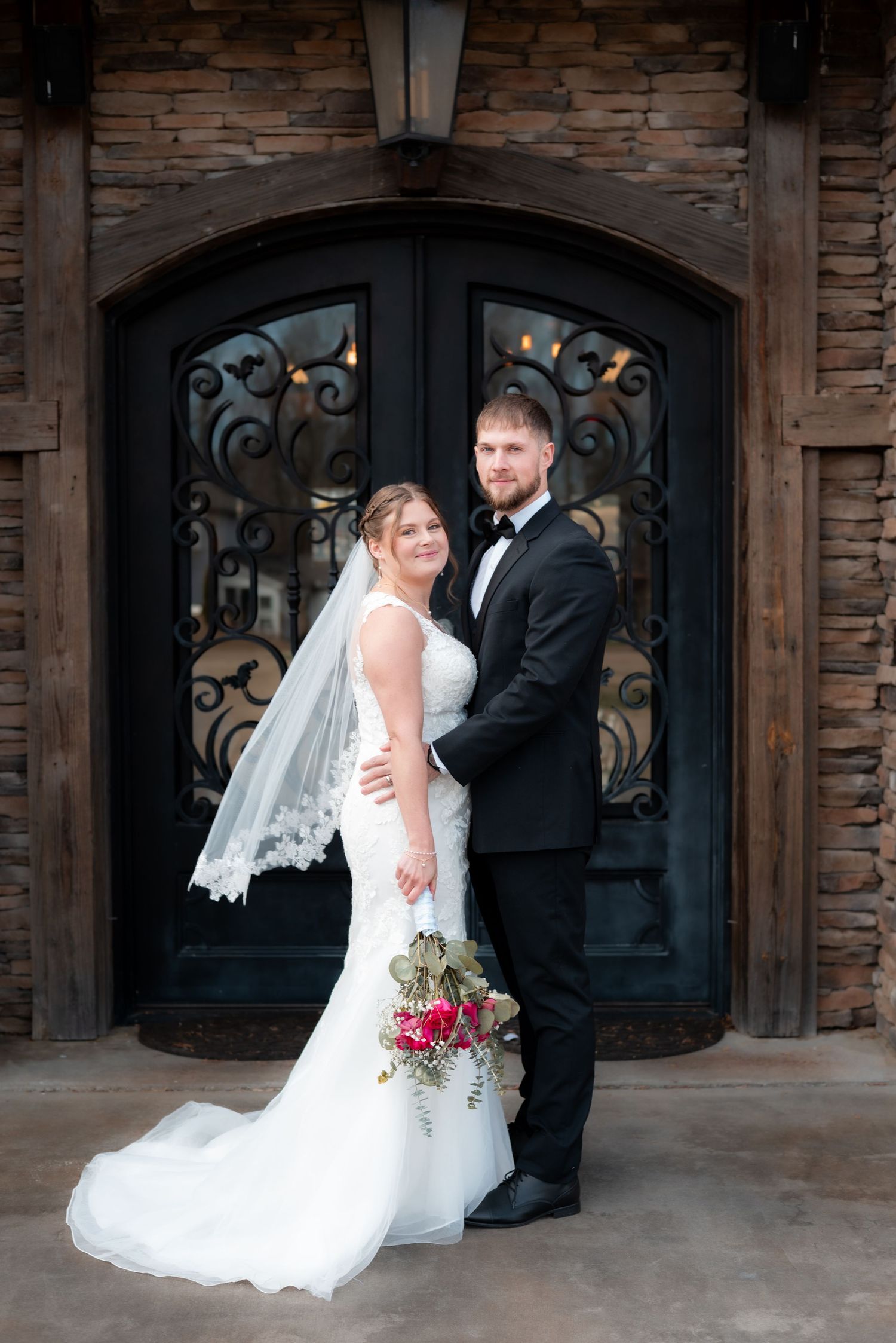 Newlyweds pose in front of an ornate iron door with stone facade.