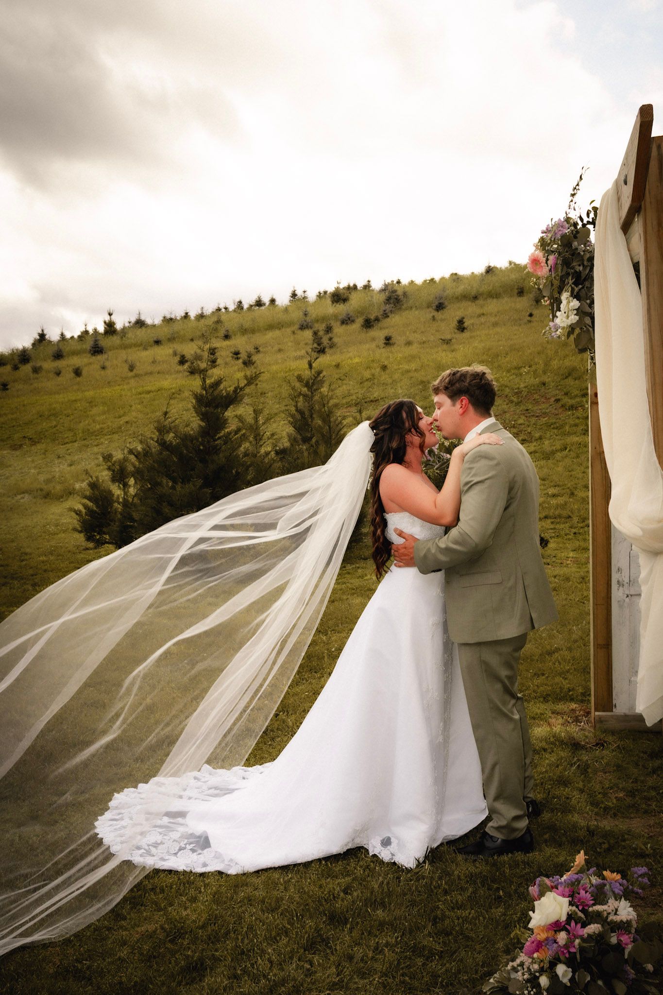 Romantic wedding couple embracing outdoors with flowing veil in the wind.