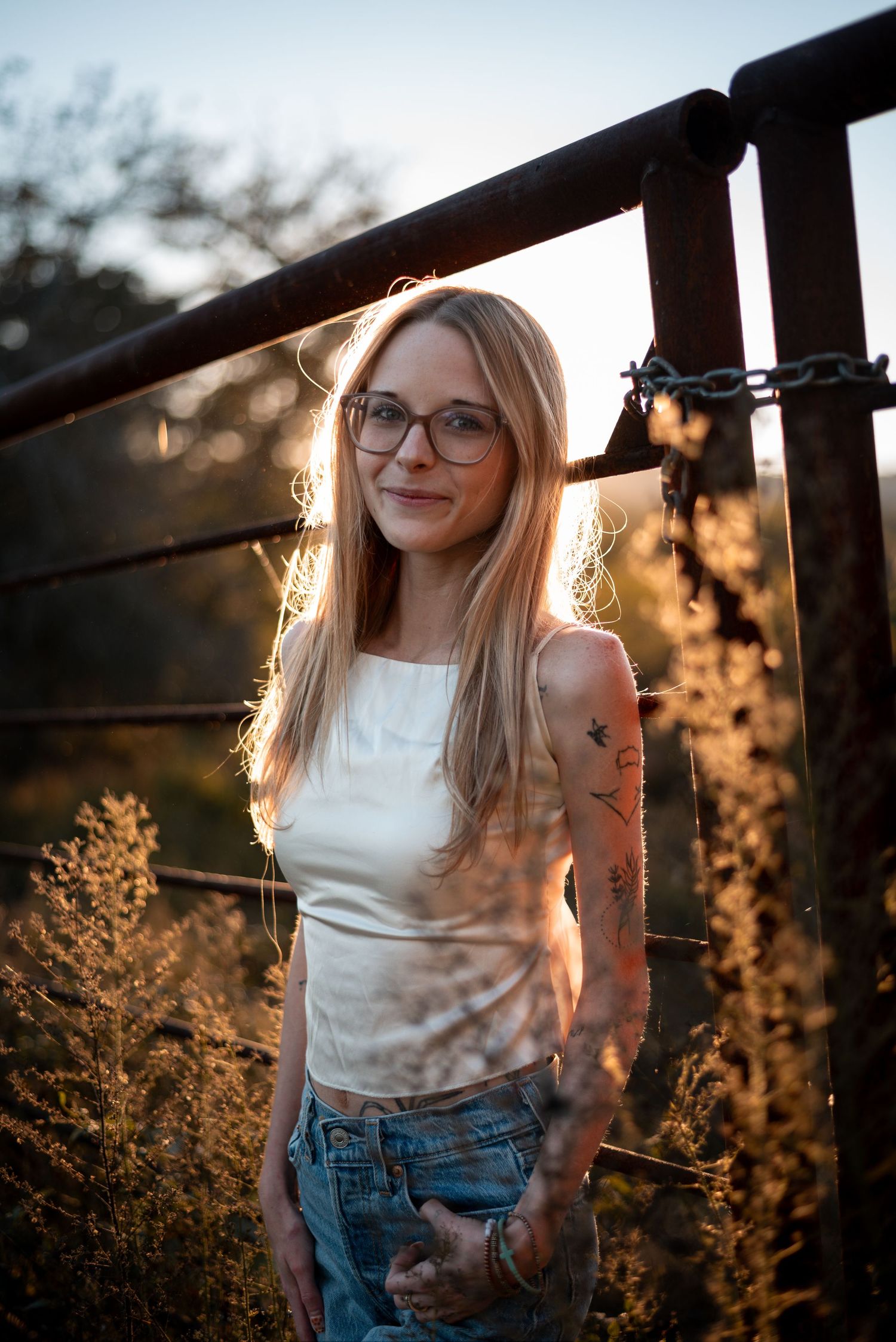 Backlit portrait against metal railings during sunset with wild grasses in soft focus.