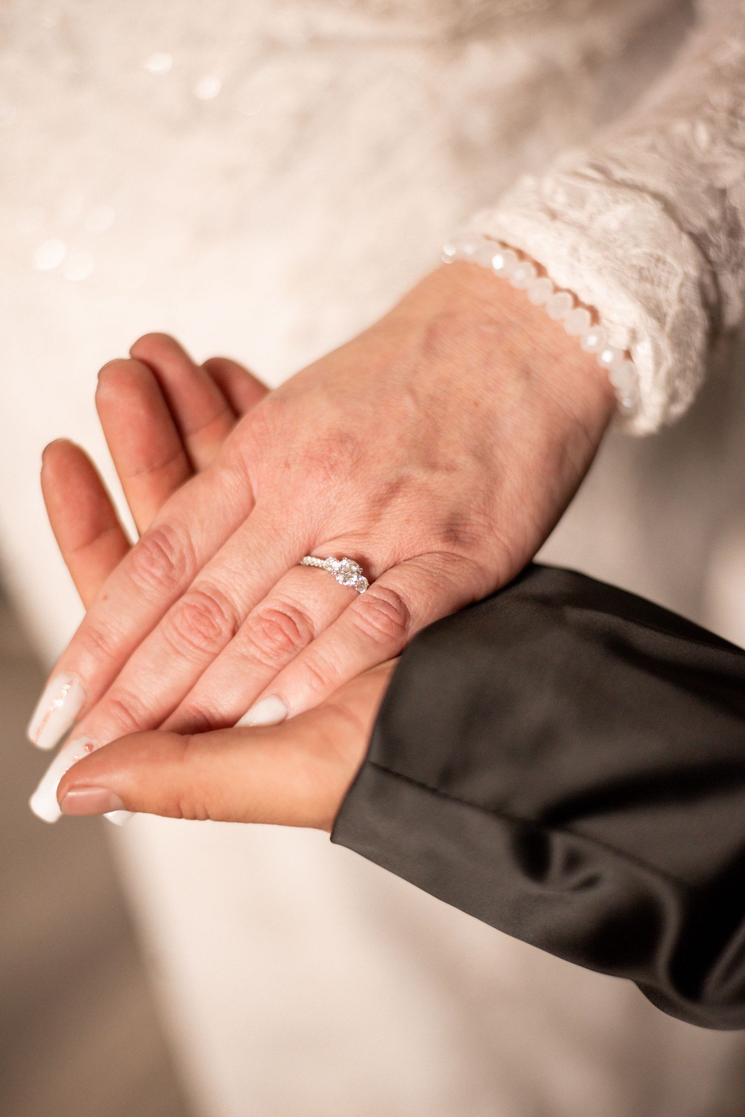 Close-up of hands showing wedding ring and French manicure against white lace dress.