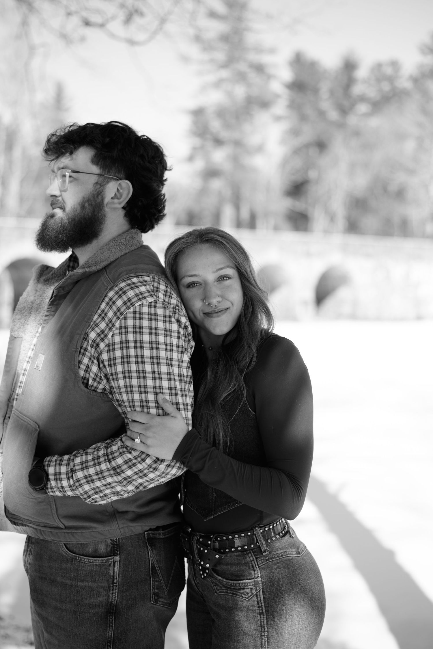Couple in casual winter wear embracing and laughing in snowy landscape.