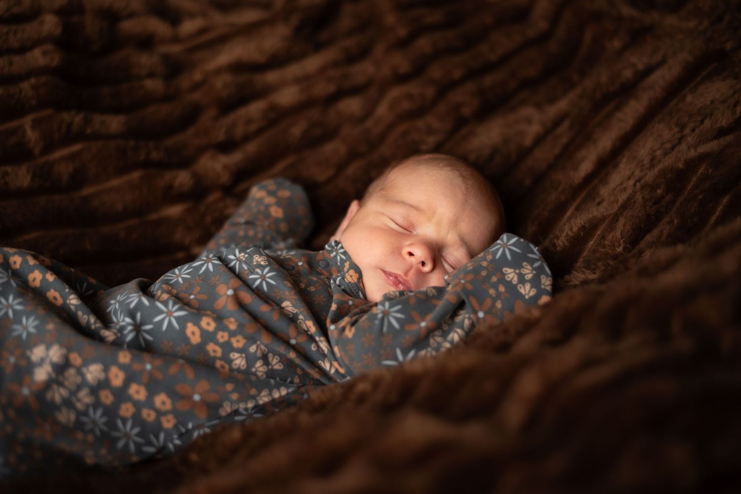 Artistic newborn photography with baby sleeping on textured brown blanket.