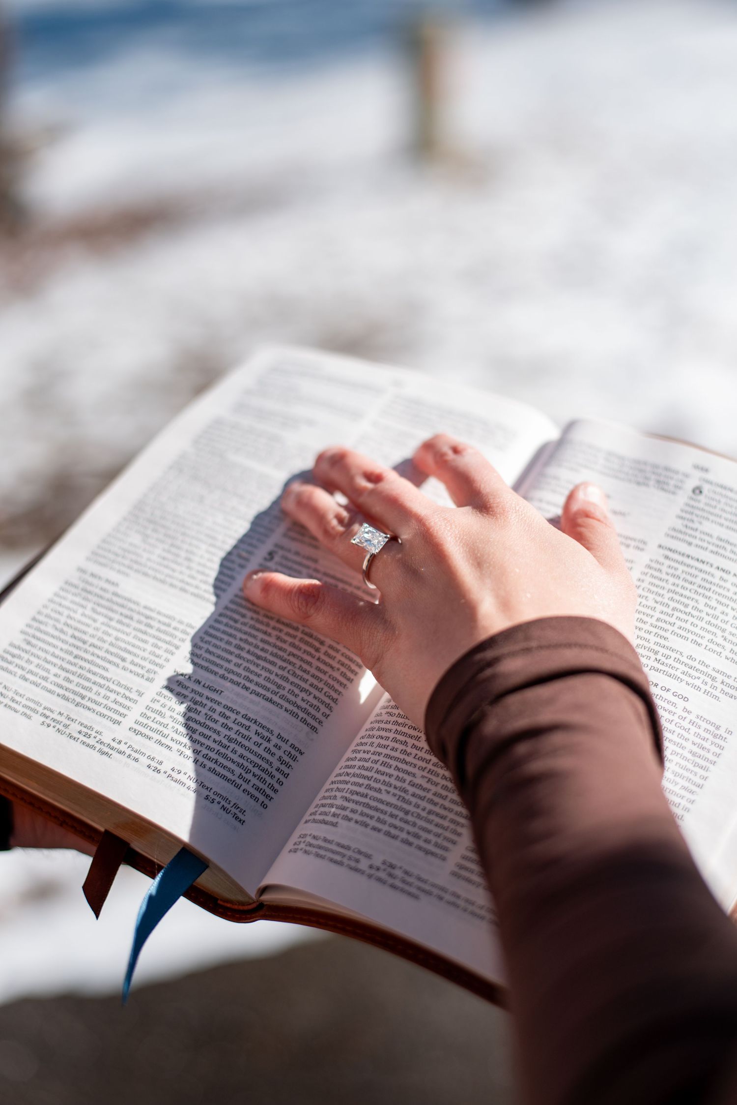 Close-up of hands with an engagement ring resting on an open book in natural light.
